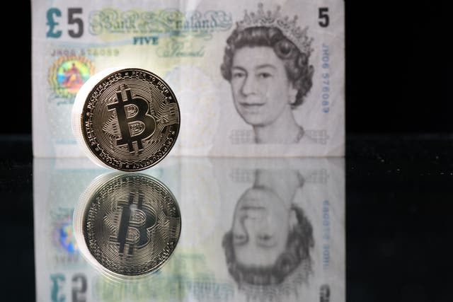 Photo taken in Paris shows a physical imitation of the Bitcoin pictured with a British five pound bank note
