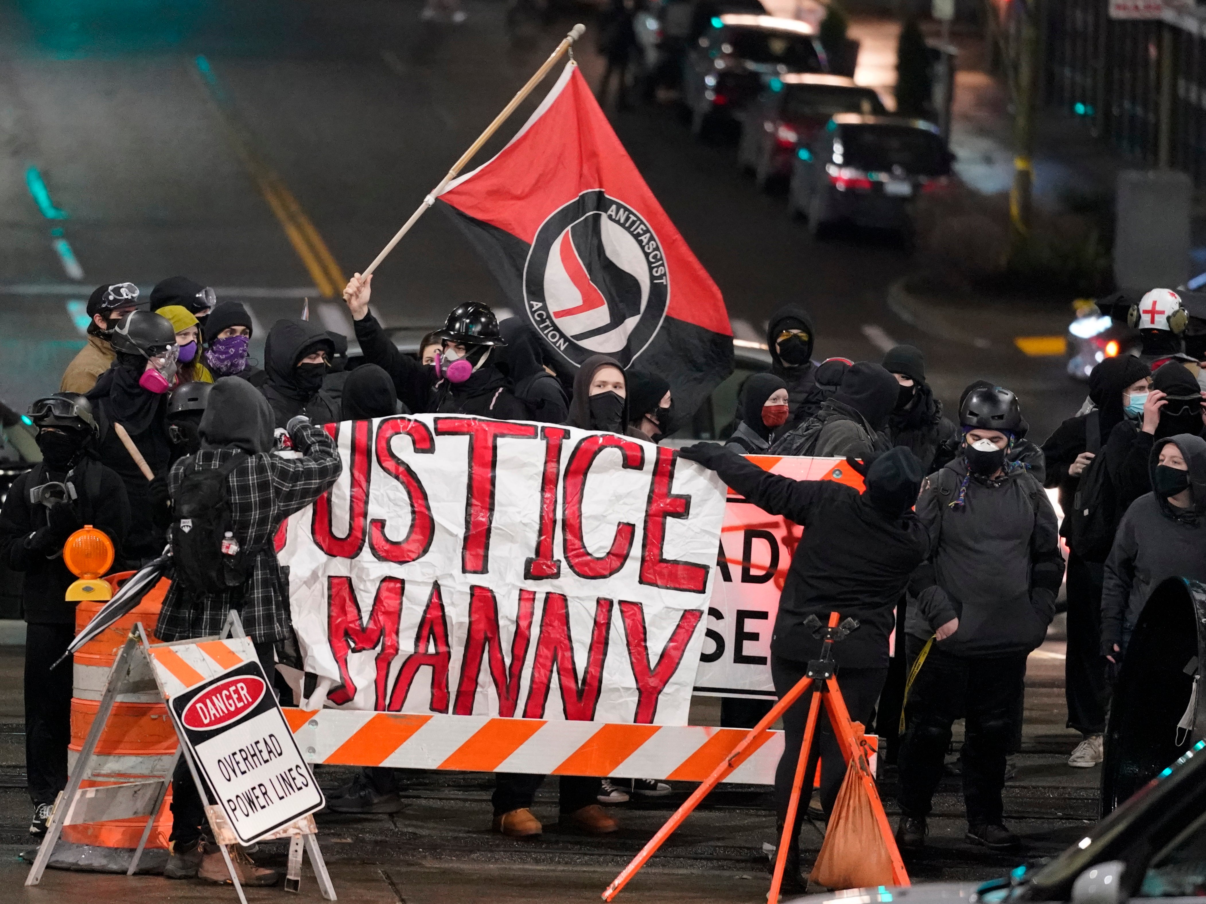 FILE - A protester carries a flag that reads "Antifascist Action" near a banner that reads "Justice for Manny," during a protest against police brutality in this Jan. 24, 2021 file photo in downtown Tacoma, Wash., south of Seattle. On Thursday, May 27, 2021, the Washington state attorney general filed criminal charges against three police officers in the death of Manuel Ellis, a Black man who died after telling the Tacoma officers who were restraining him he couldn't breathe. (AP Photo/Ted S. Warren, File)