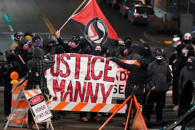FILE - A protester carries a flag that reads "Antifascist Action" near a banner that reads "Justice for Manny," during a protest against police brutality in this Jan. 24, 2021 file photo in downtown Tacoma, Wash., south of Seattle. On Thursday, May 27, 2021, the Washington state attorney general filed criminal charges against three police officers in the death of Manuel Ellis, a Black man who died after telling the Tacoma officers who were restraining him he couldn't breathe. (AP Photo/Ted S. Warren, File)