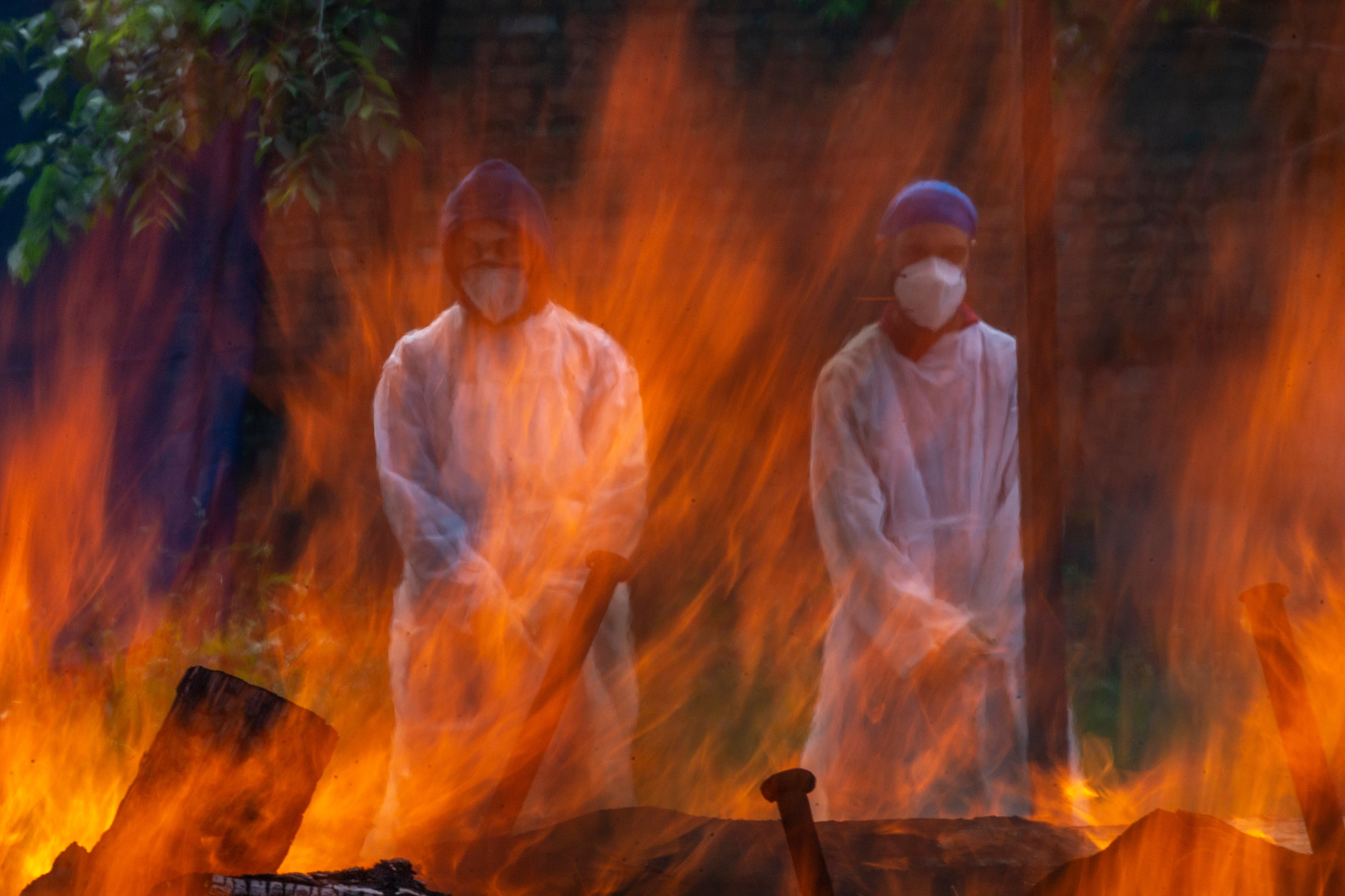 <p>Relatives in protective suits stand next to the burning pyre of a person who died of Covid at a Srinagar crematorium</p>