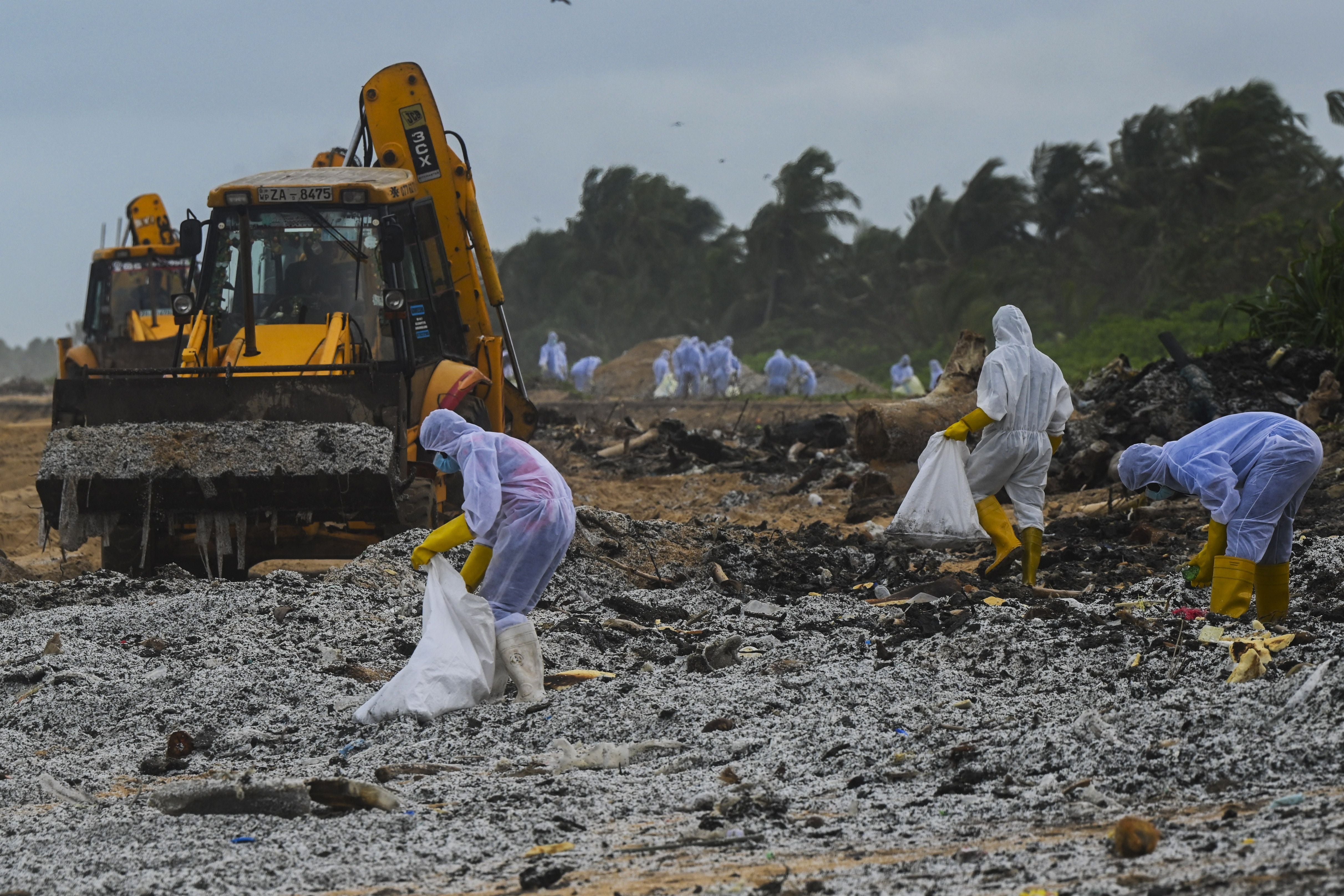 <p>Sri Lankan Navy soldiers with the help of heavy machinery work to remove debris washed ashore from the Singapore-registered container ship MV X-Press Pearl, which has been burning for the eighth consecutive day in the sea off Sri Lanka's Colombo Harbour, on a beach in Colombo on May 28, 2021. </p>