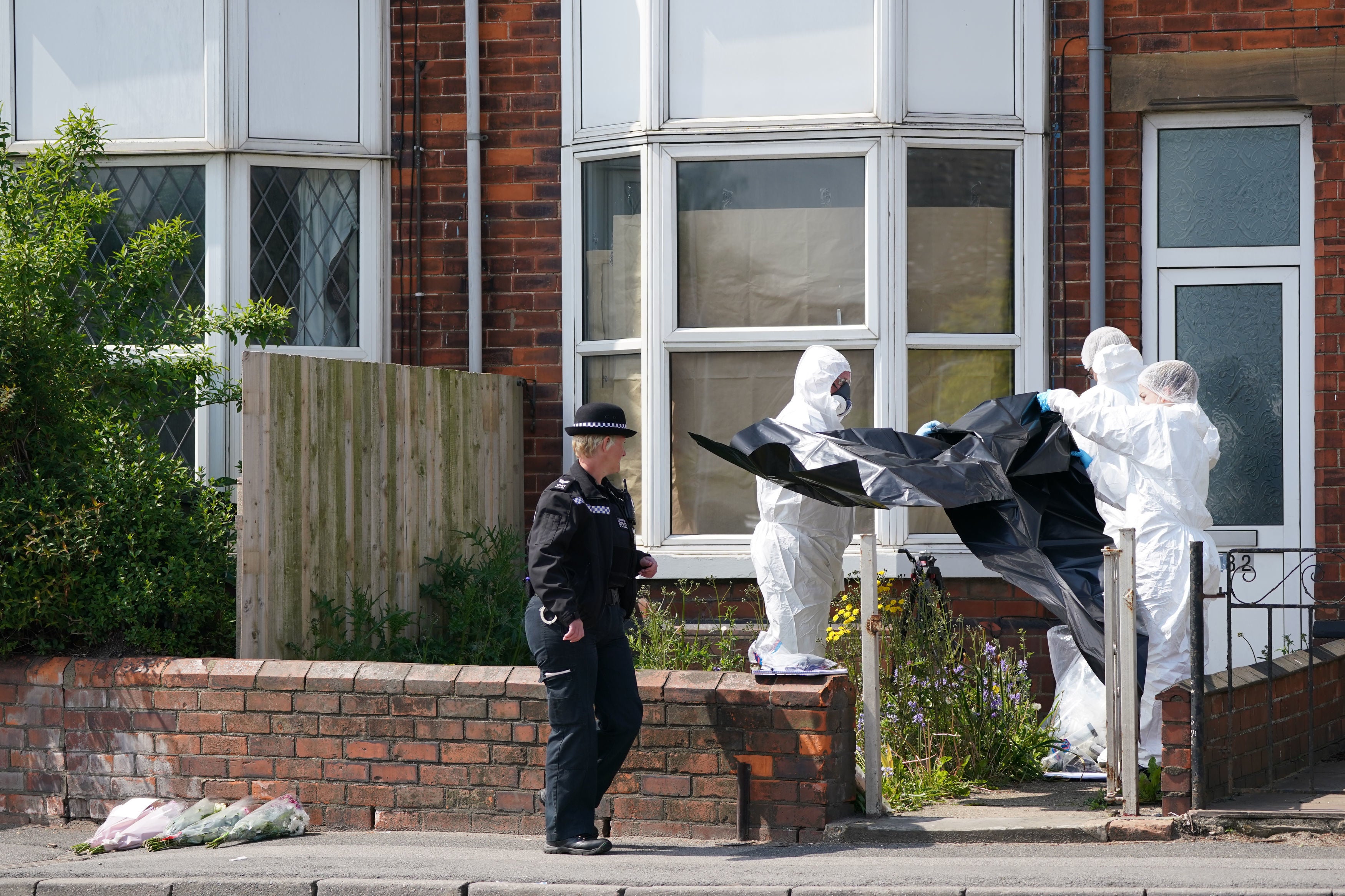 Floral tributes are seen as forensic experts examine the murder scene