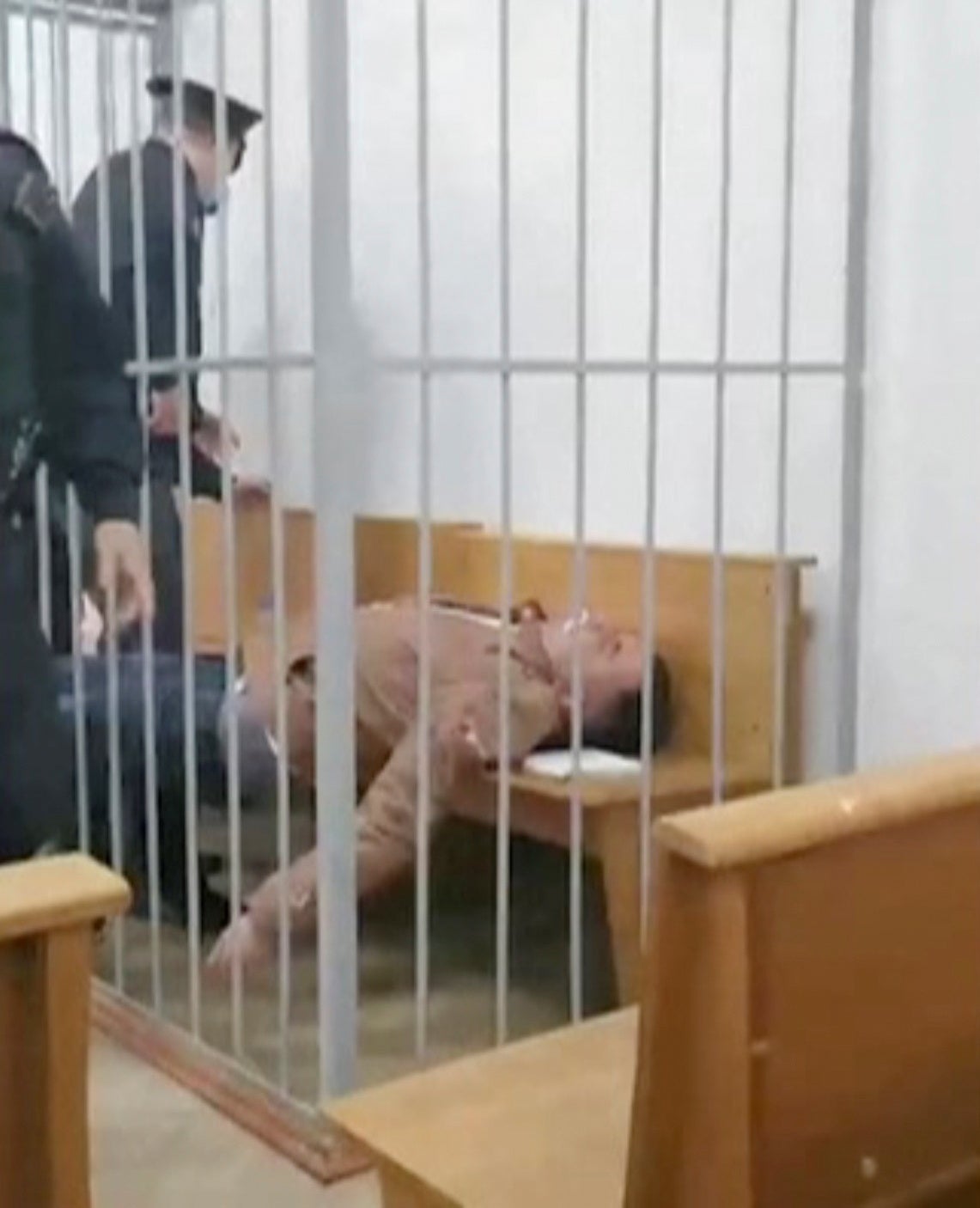 <p>Belarusian prisoner Stepan Latypov lies on a bench after an attempt to cut his throat inside the  cage dock in a court in Minsk</p>