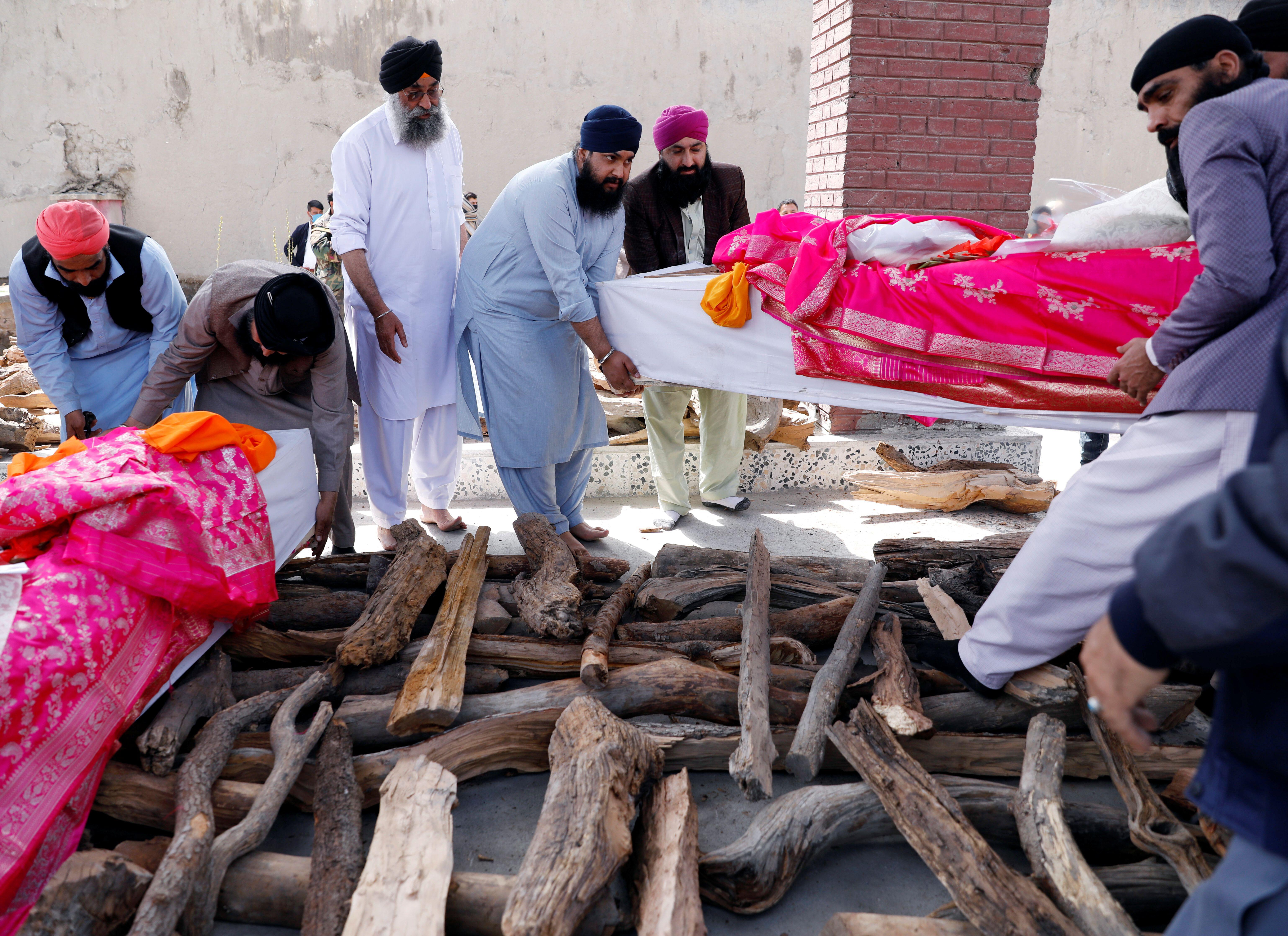 Afghan Sikh men carry coffins before lighting the funeral pyre for the victims killed during the attack on the temple