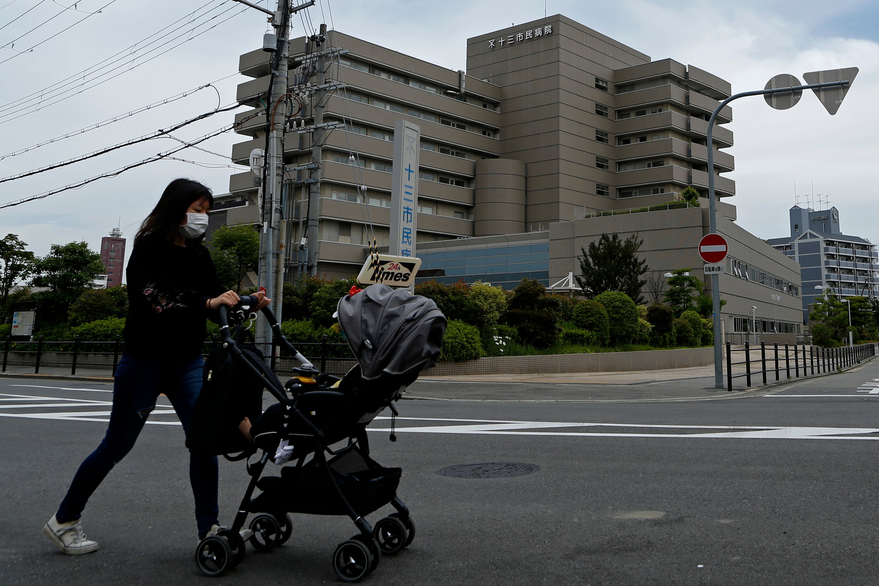 A woman wearing a protective face mask pushes a baby stroller outside the Osaka City Juso Hospital