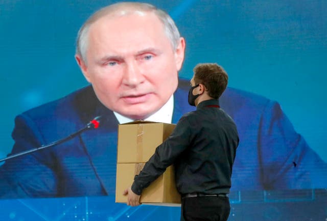 <p>A man carries boxes as Russian President Vladimir Putin seen on a screen in the background at the St Petersburg International Economic Forum </p>