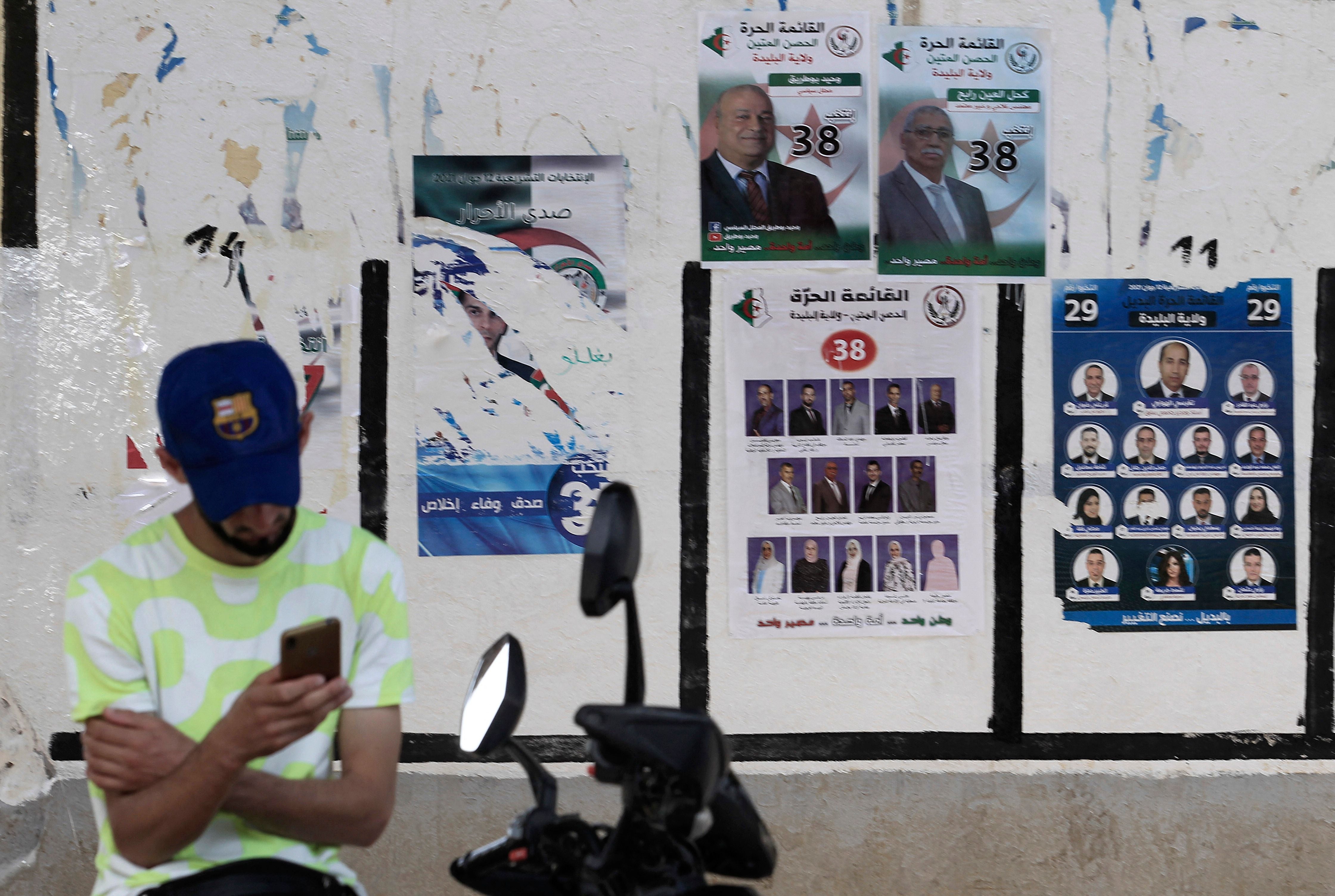An Algerian man checks his mobile phone next to election posters in the capital Algiers ahead of the upcoming elections scheduled for June 12