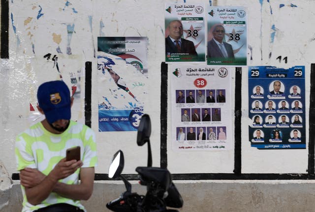 <p>An Algerian man checks his mobile phone next to election posters in the capital Algiers ahead of the upcoming elections scheduled for June 12</p>