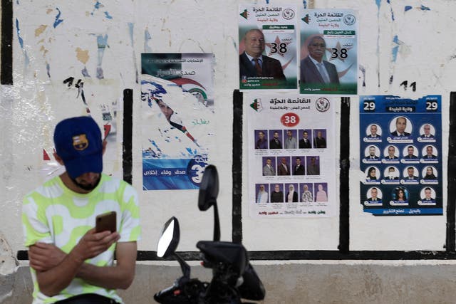 <p>An Algerian man checks his mobile phone next to election posters in the capital Algiers ahead of the upcoming elections scheduled for June 12</p>