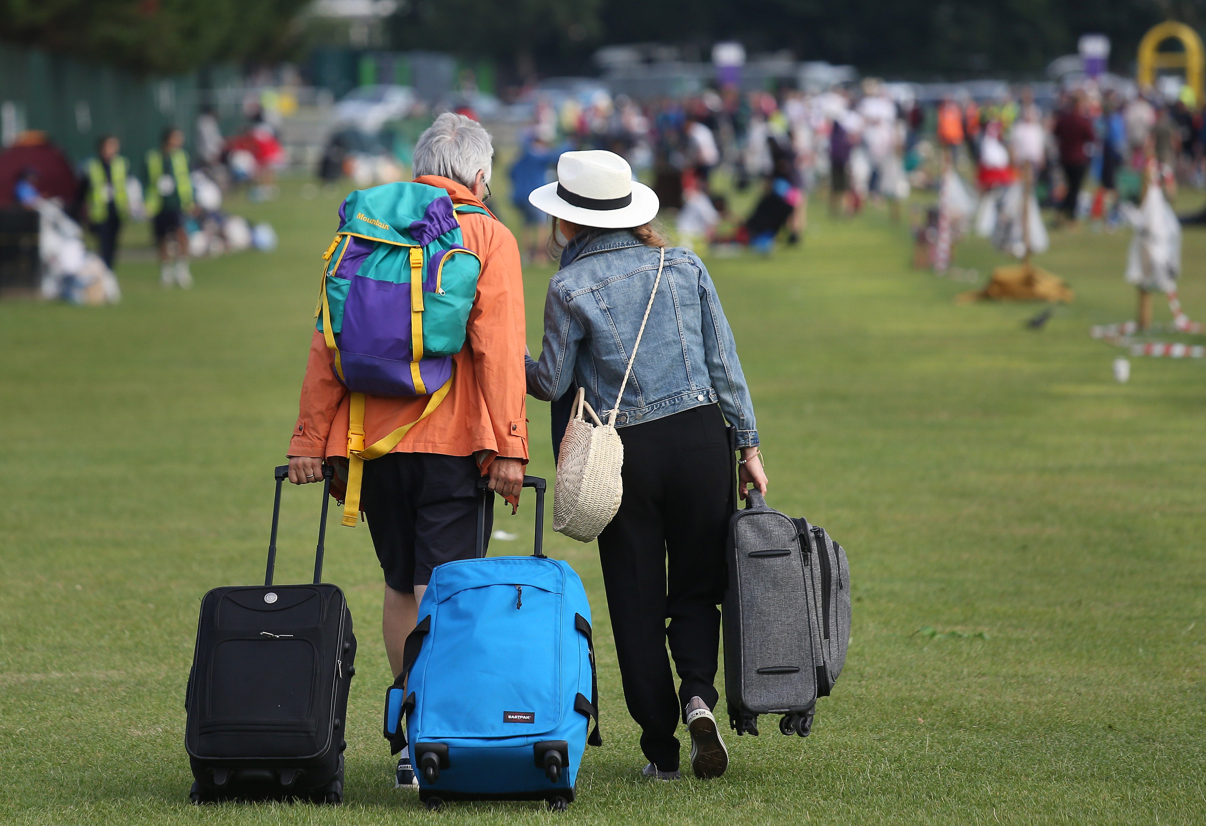 A man and woman pull suitcases across grass