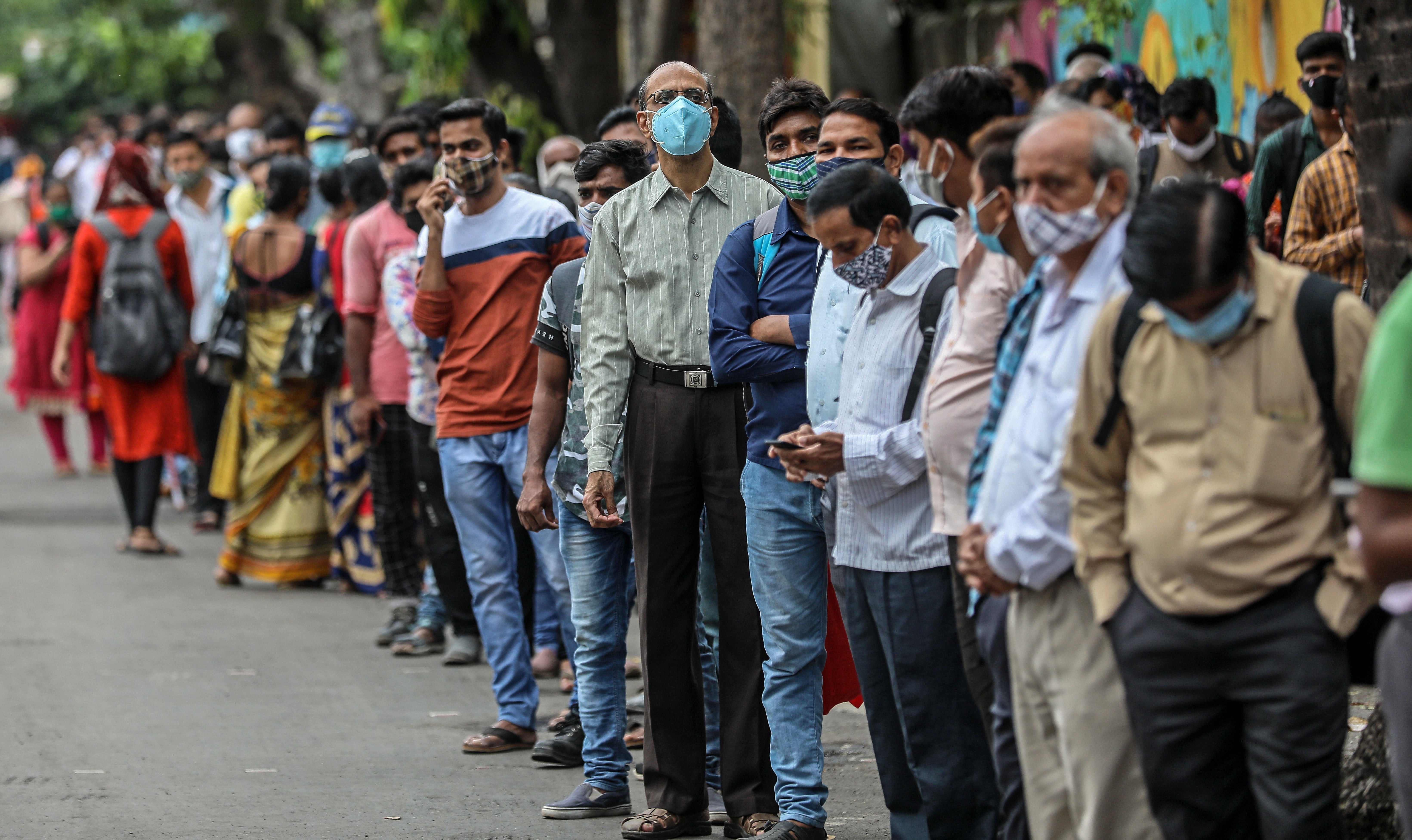 People stand in a queue as they wait for public transport at a bus stop in Mumbai, India, on 8 June, 2021