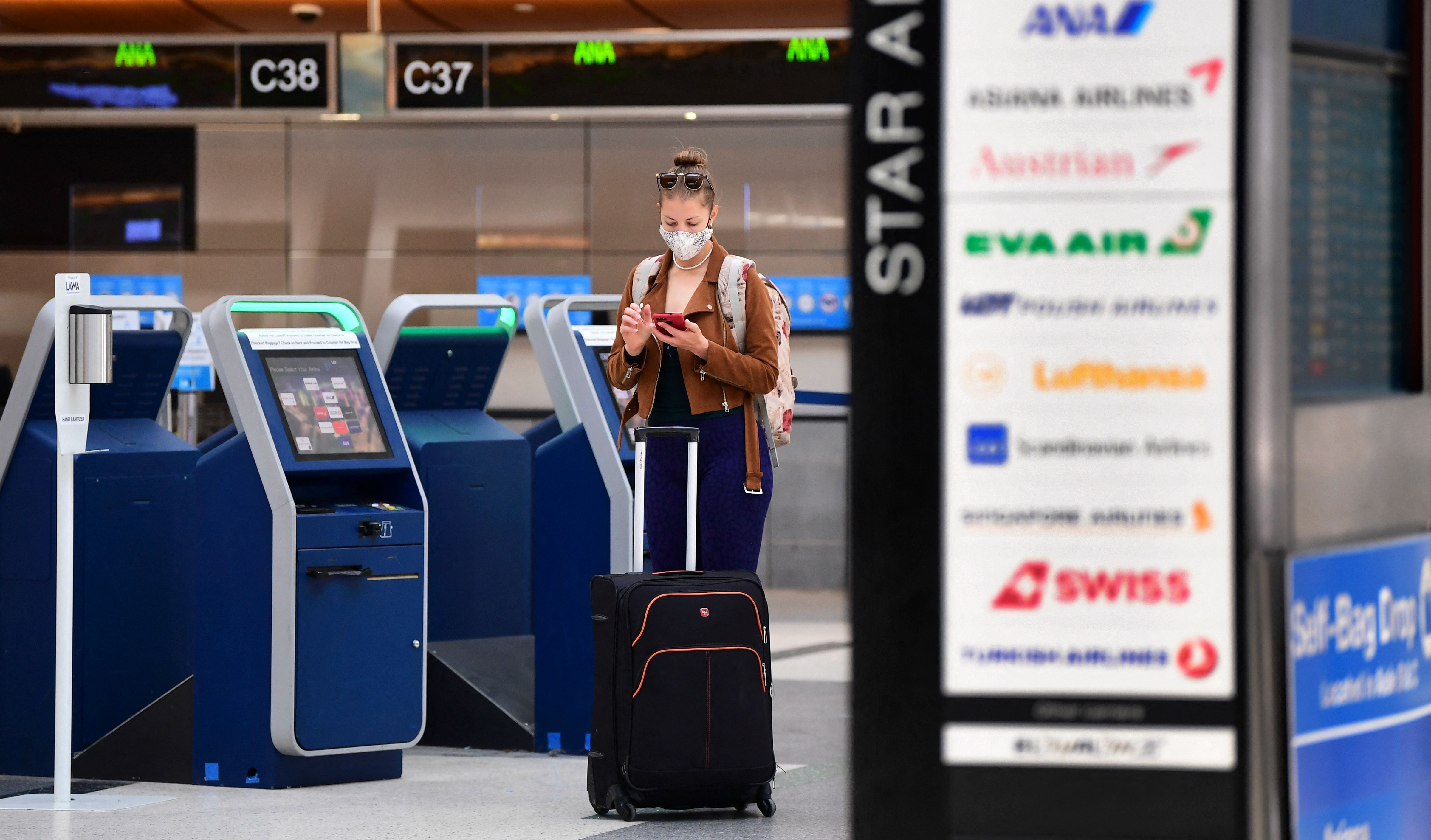 A woman checks her cellphone by self check-in kiosks on the departures level of Los Angeles International Airport (LAX) on May 27, 2021 in Los Angeles.