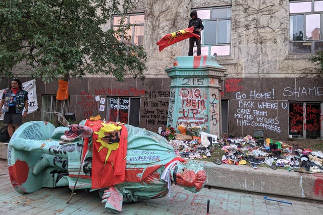<p>A man waving the Mohawk Warrior Society flag stands on the pedestal of the toppled statue of Egerton Ryerson, one of the architects of indigenous boarding school system, in Toronto on June 6, 2021. </p>