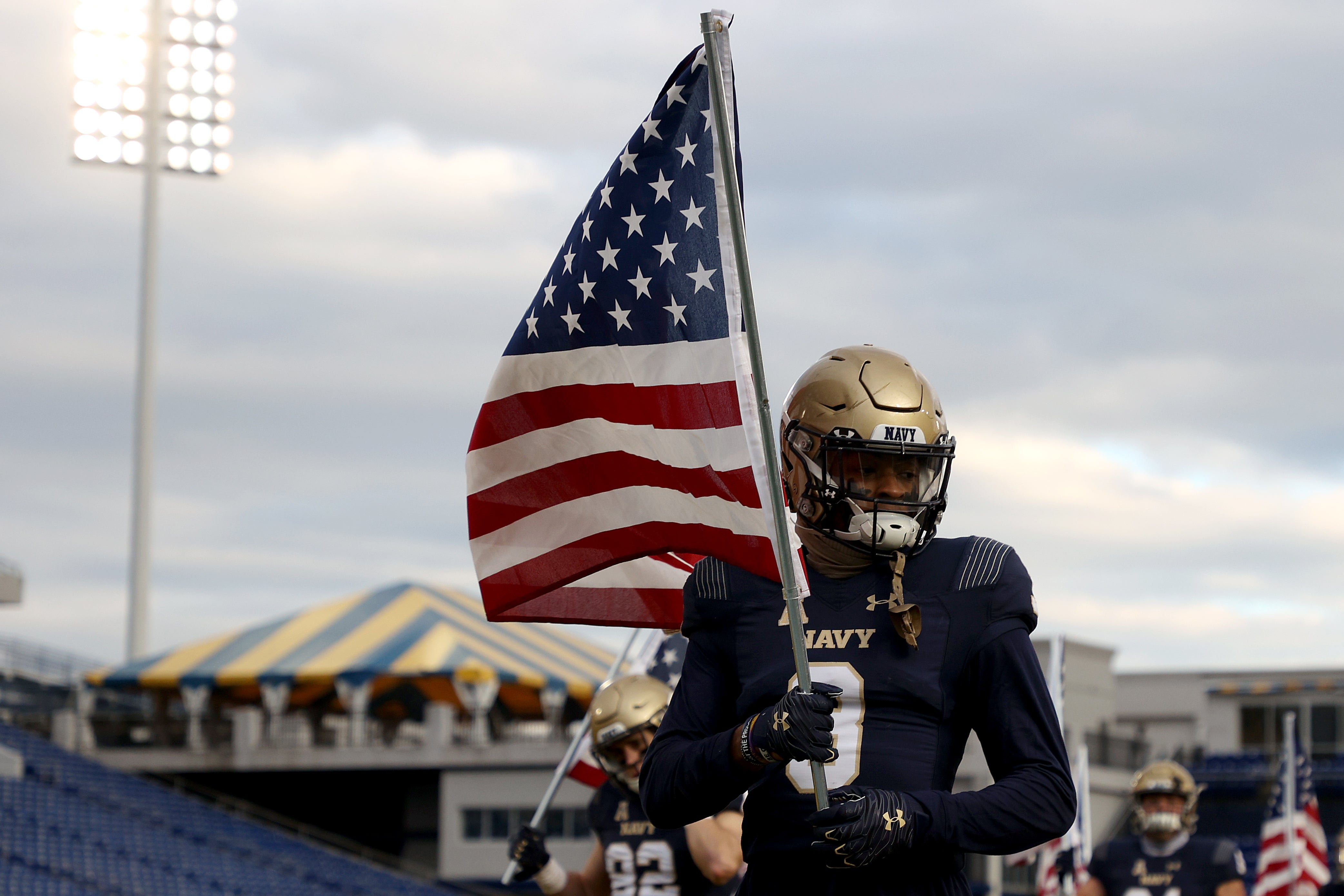 ANNAPOLIS, MARYLAND - DECEMBER 05: Cameron Kinley #3 of the Navy Midshipmen carries an American flag as the team takes the field against the Tulsa Golden Hurricane at Navy-Marine Corps Memorial Stadium on December 05, 2020 in Annapolis, Maryland.