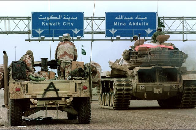 <p>A US Humvee and a Saudi tank pass under a sign directing them to Kuwait City in February 1991 during the Desert Storm offensive</p>