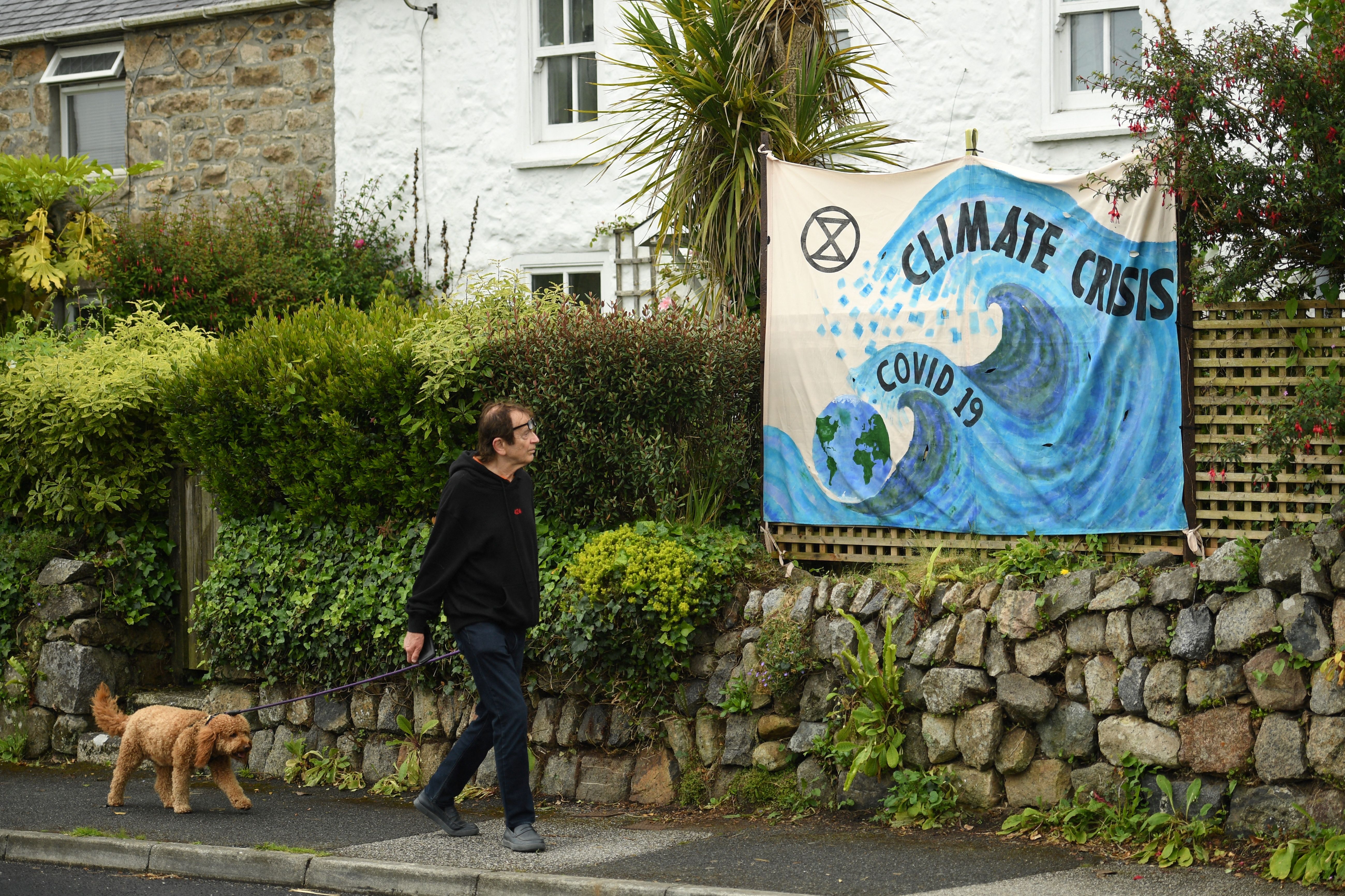 A man walks past a banner displayed on a garden wall in St Ives, Cornwall, ahead of the three-day G7 summit being held from 11-13 June