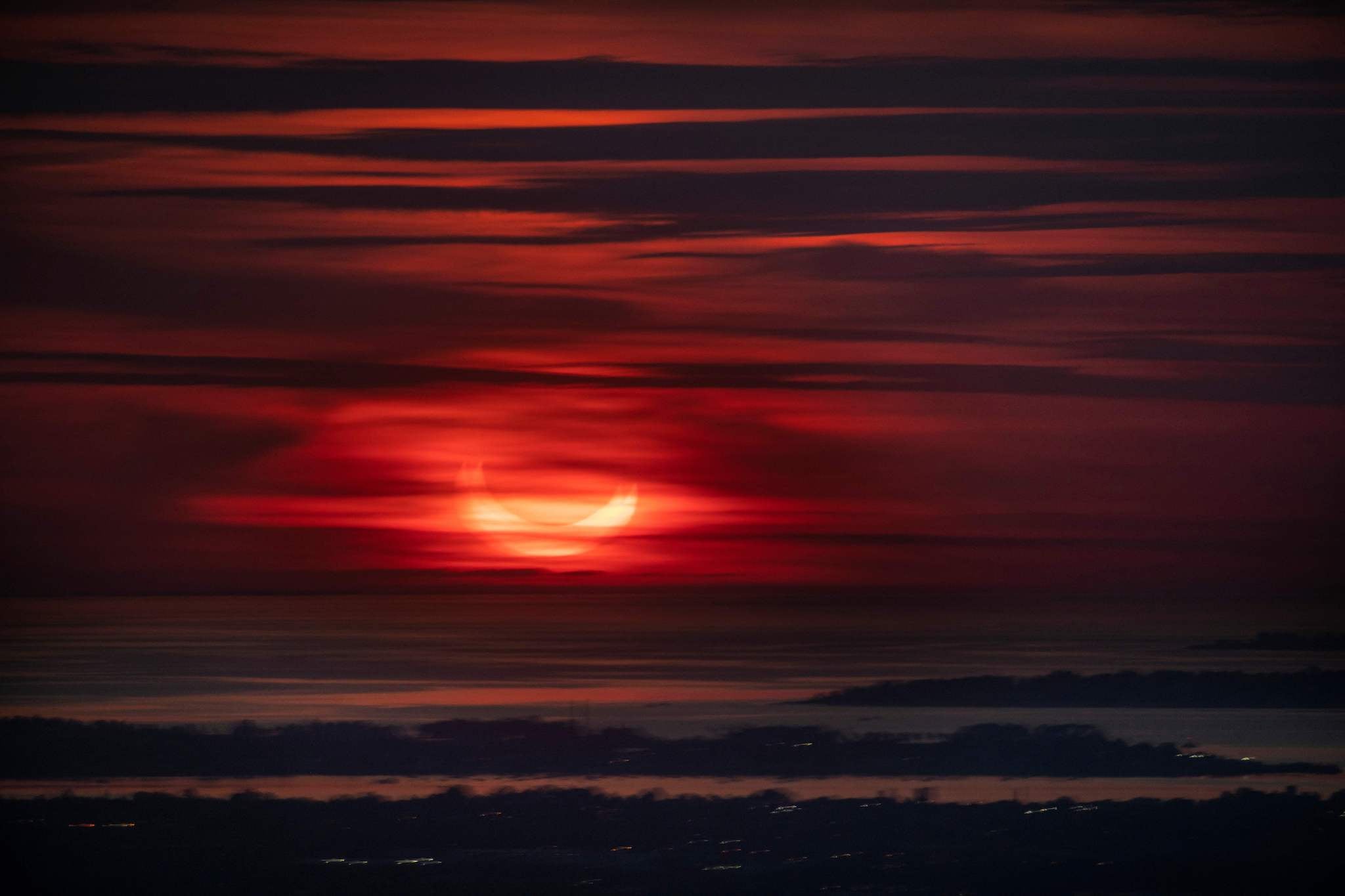 The sun rises partially eclipsed in this view taken from behind a window (hence the doubling effect) of Summit One Vanderbilt, a high rise in New York City