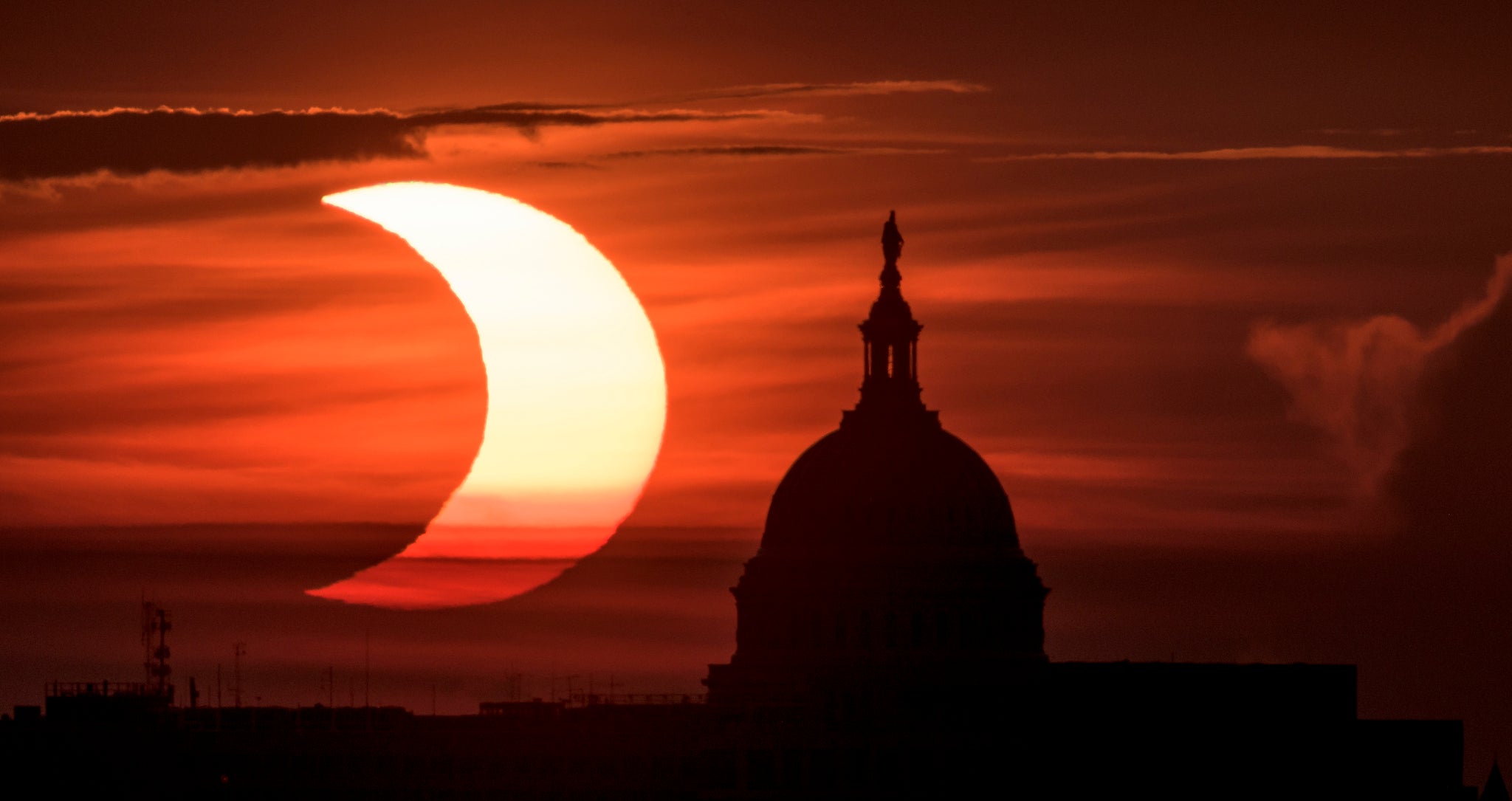 The partial solar eclipse is seen as the sun rises to the left of the United States Capitol building