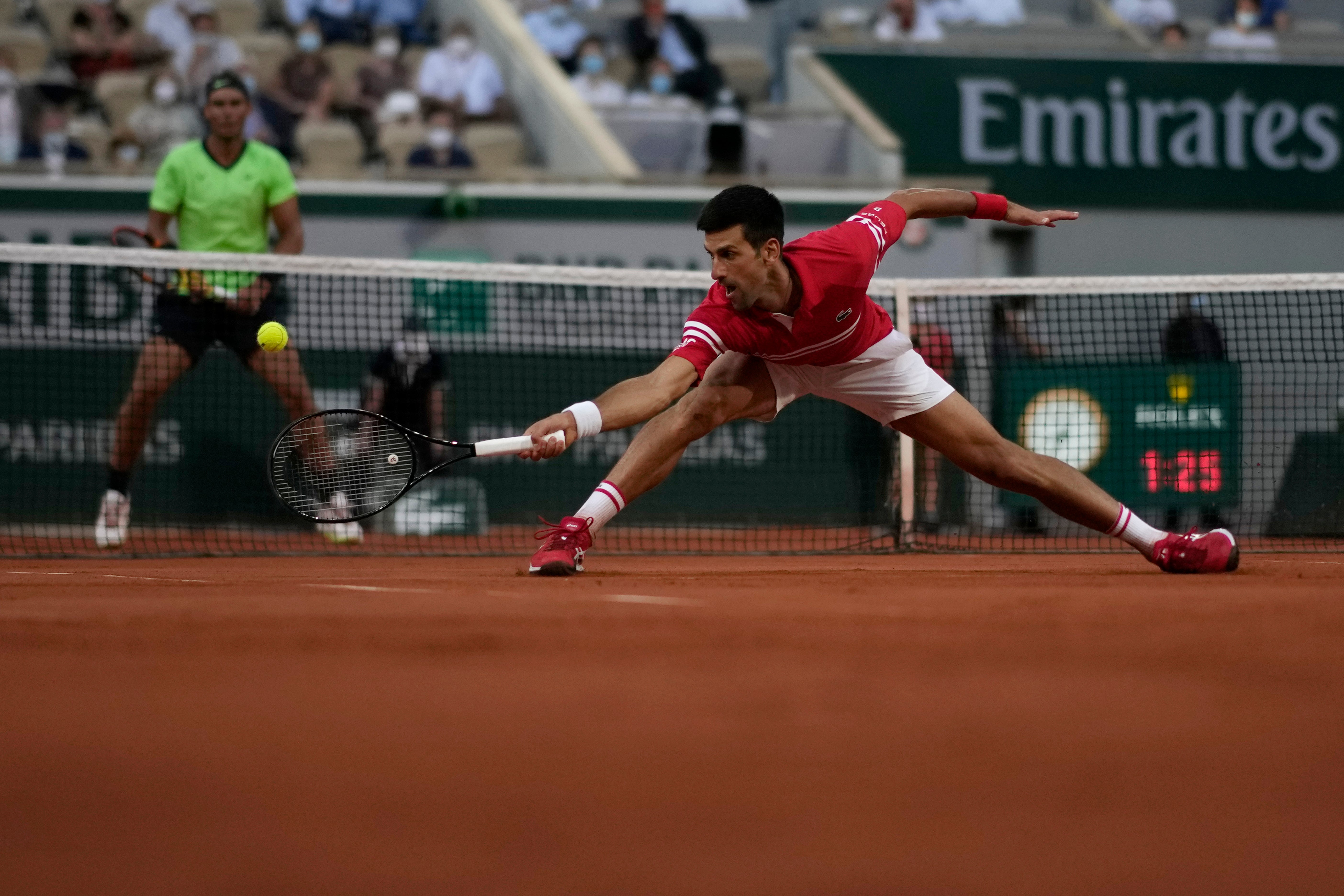 Novak Djokovic stretches for a backhand with Rafael Nadal watching