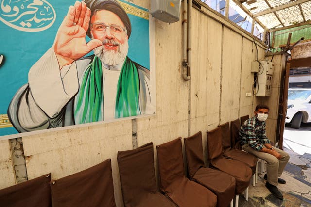<p>An Iranian sits under a poster of presidential candidate Ebrahim Raisi at a campaign office in Tehran on 7 June</p>