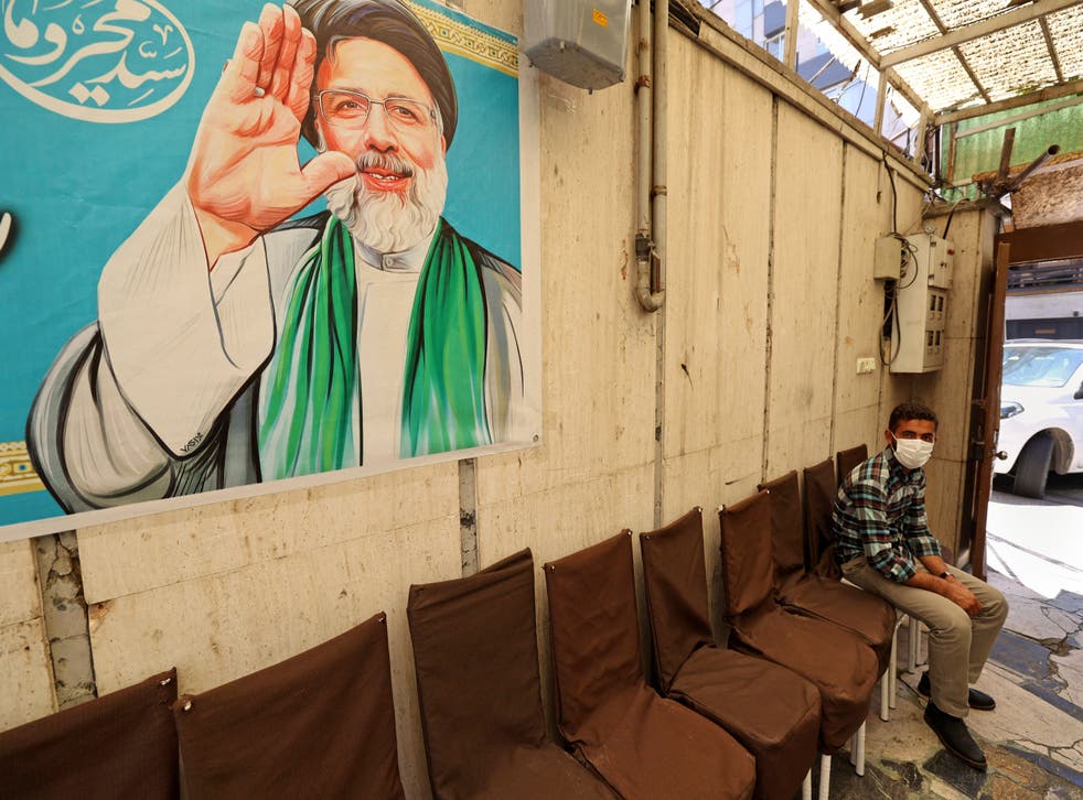 <p>An Iranian sits under a poster of presidential candidate Ebrahim Raisi at a campaign office in Tehran on 7 June</p>