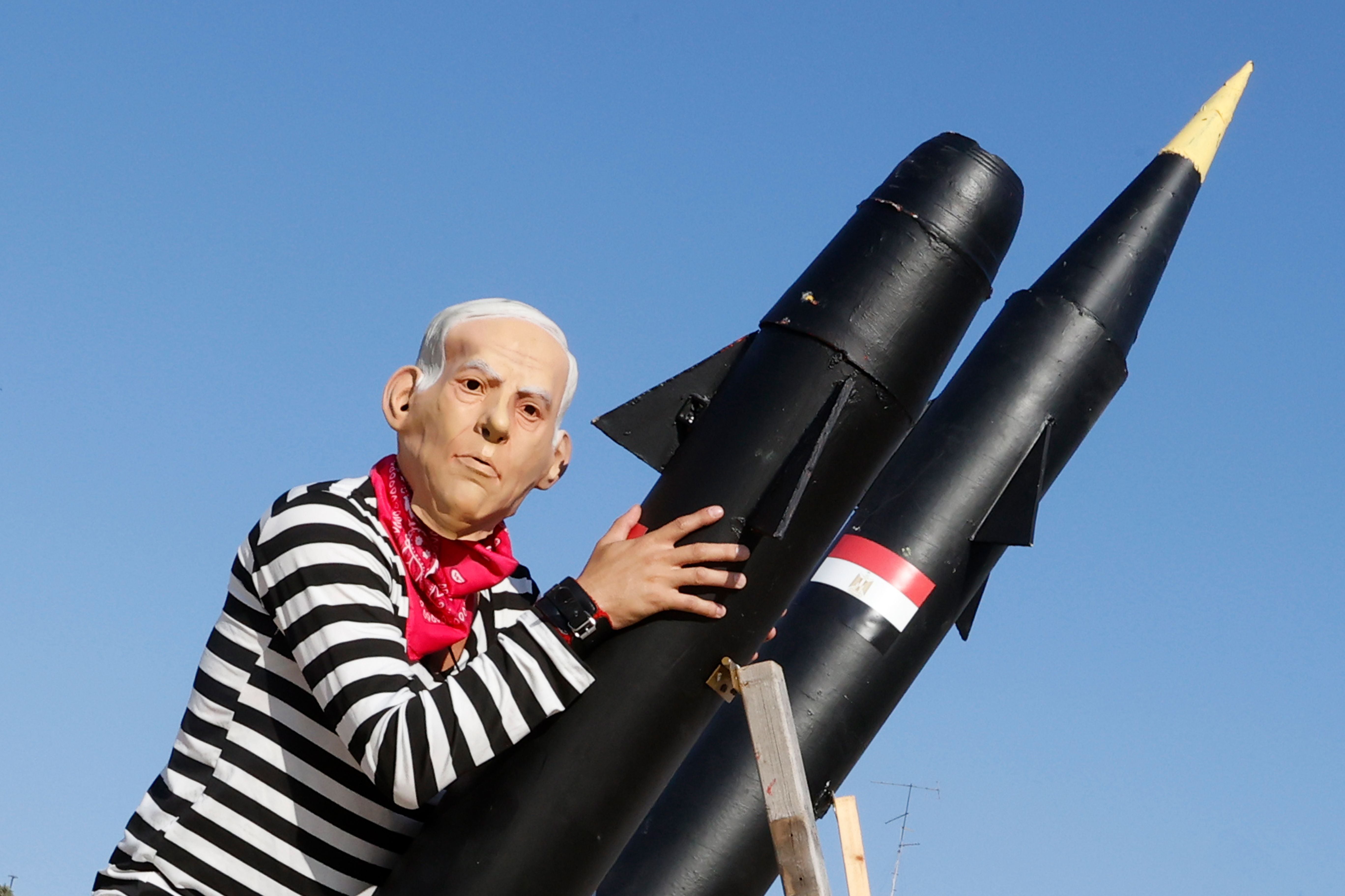 An Israeli protester wearing a mask of Netanyahu holds a mock rocket during a demonstration in 2020