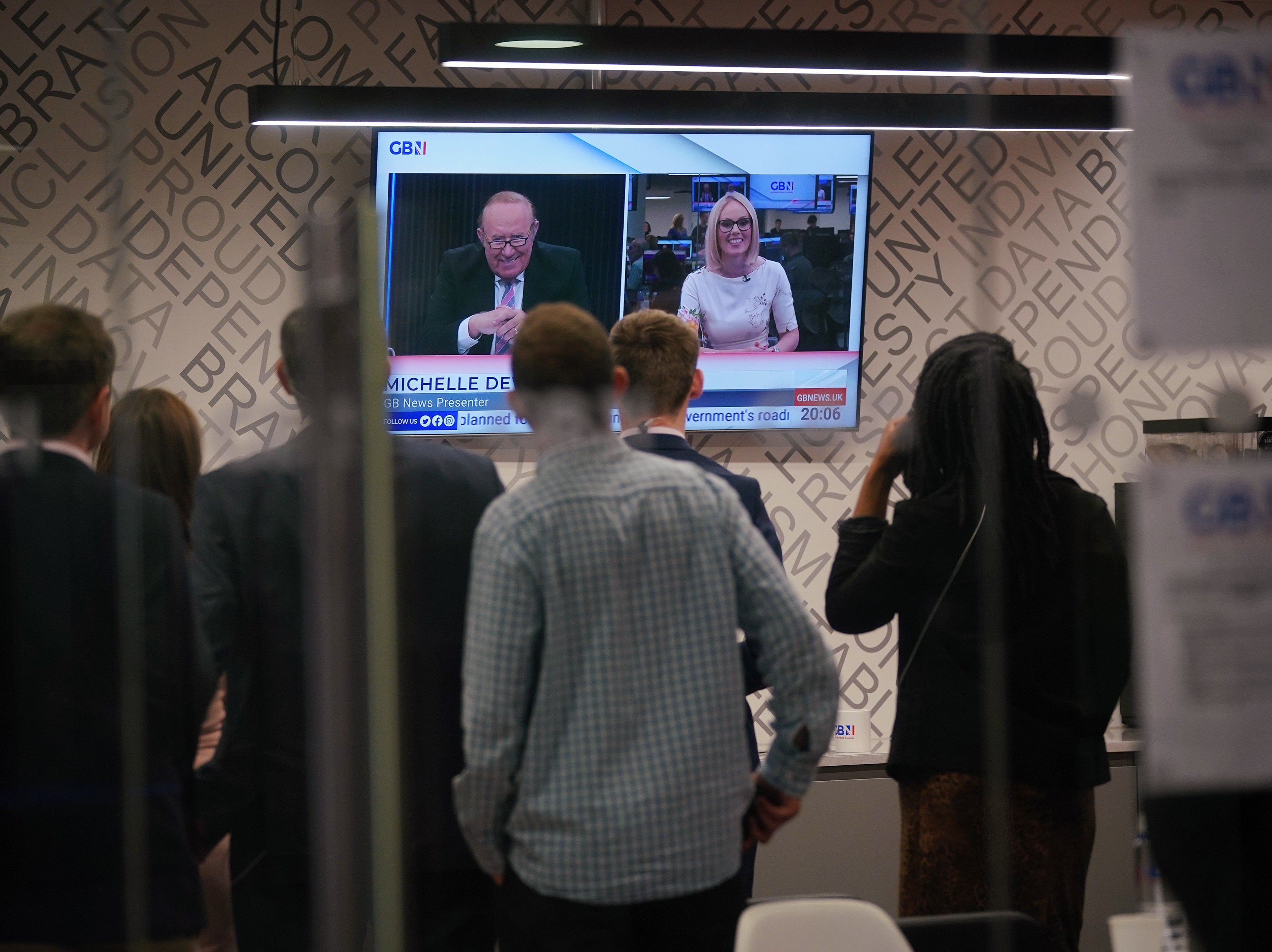 Staff in the green room watching a television screen showing presenters Andrew Neil and Michelle Dewberry broadcast from a studio, during the launch event for new TV channel GB News