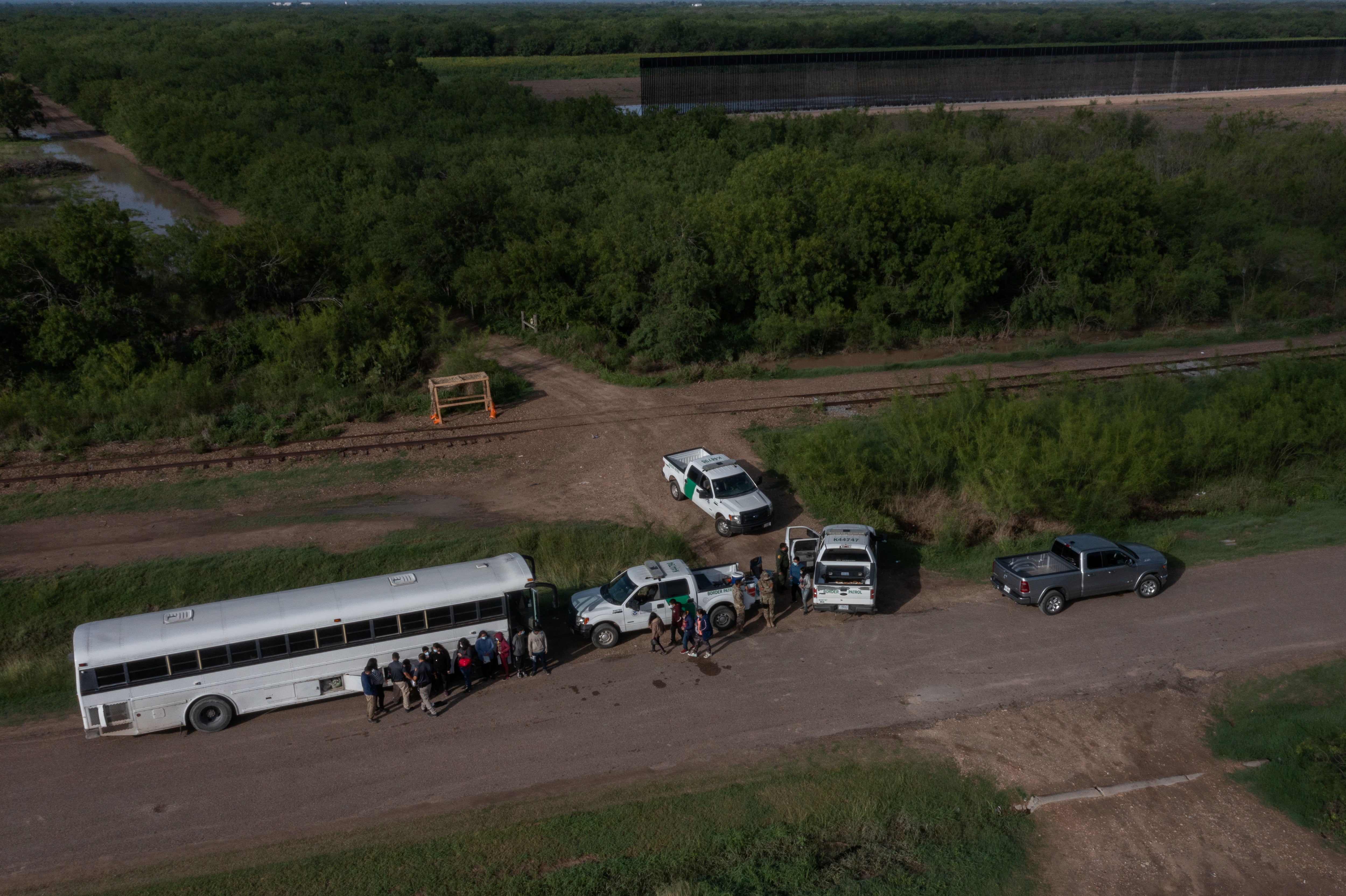 <p>File image: Part of an incomplete border wall is seen in the background as asylum-seeking migrants from Central America line-up outside of a US board patrol bus after crossing the Rio Grande river into the United States from Mexico in La Joya, Texas, US, 20 May, 2021</p>