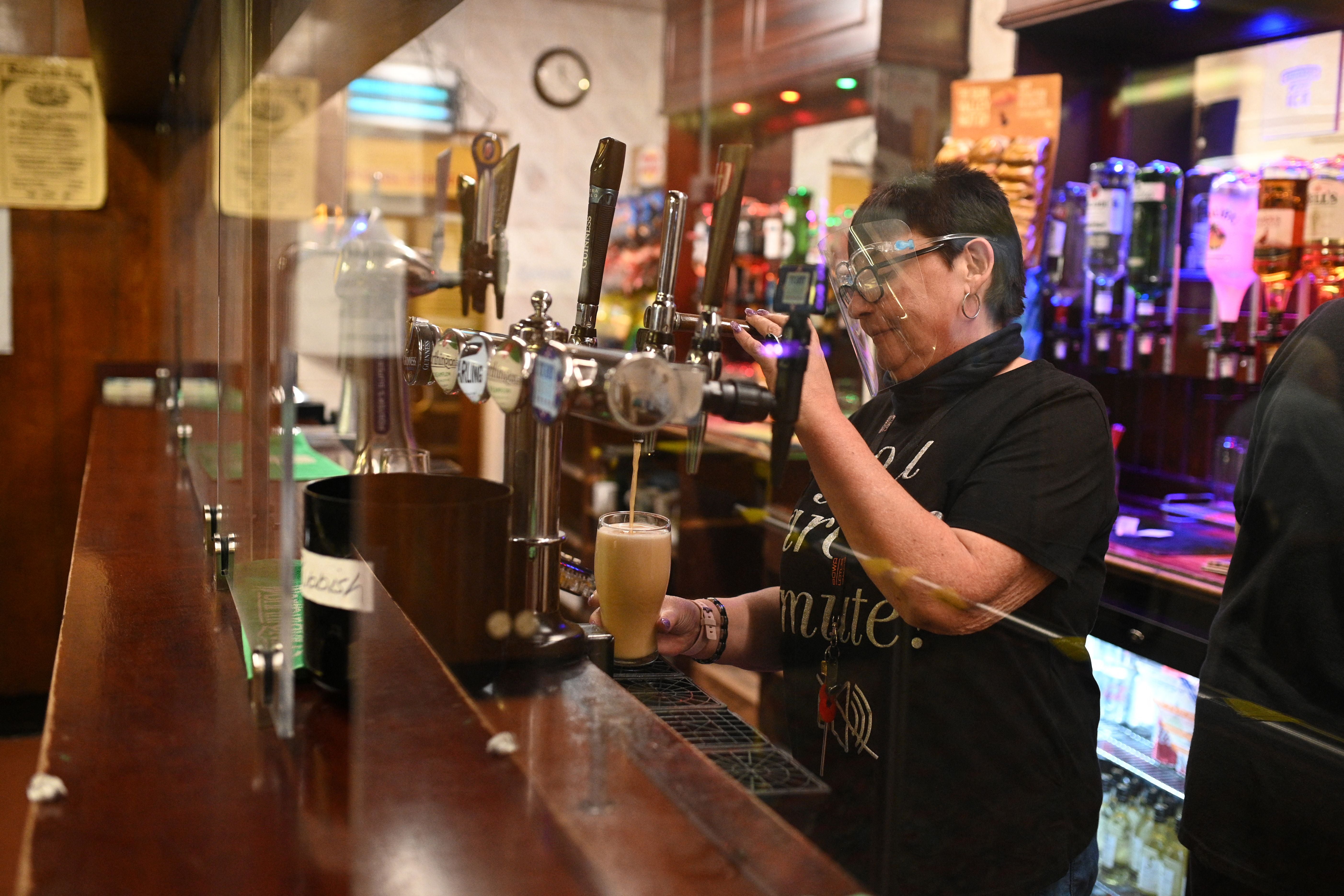 <p>A member of staff pours a drink behind a perspex screen at the Harehills Labour Club Leeds on 17 May, 2021. </p>