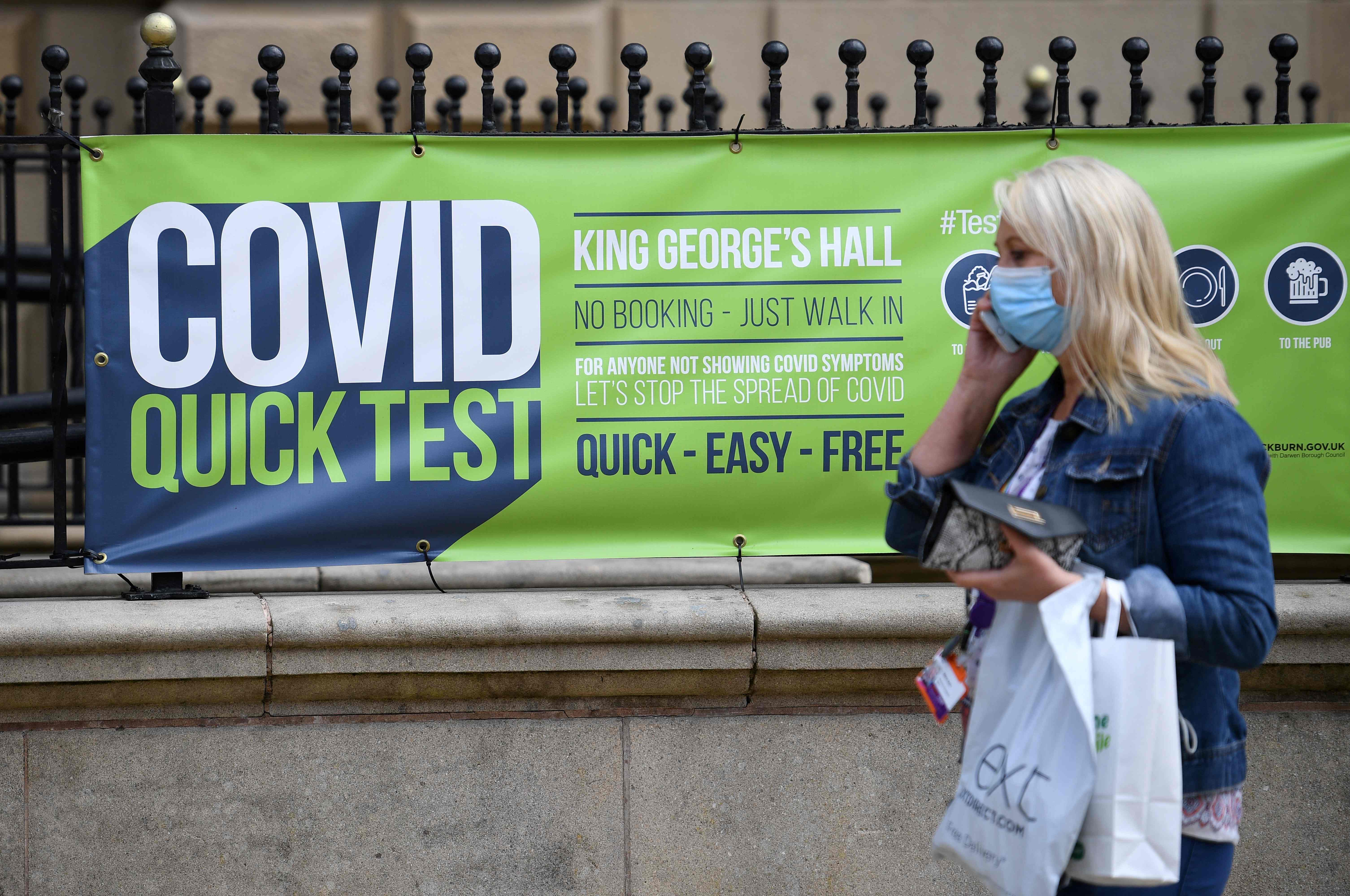 A person wearing a face covering walks past a sign for a walk-in Covid-19 testing centre in Blackburn on Wednesday