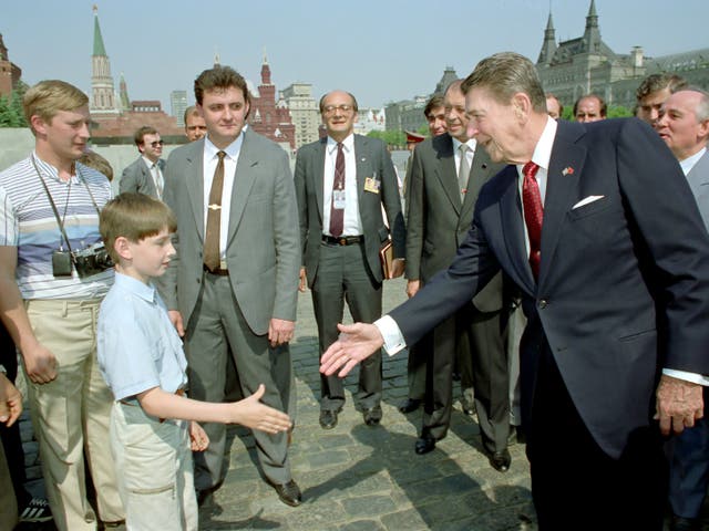 <p>Ronald Reagan extends his hand to a boy as Mikhail Gorbachev (R) looks on during a tour of Moscow’s Red Square - could it also show a young Vladimir Putin (left, with camera) posing as a tourist?</p>