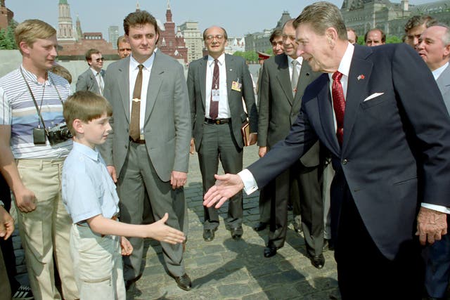 <p>Ronald Reagan le da la mano a un niño mientras Mikhail Gorbachev (der.) observa durante un recorrido por la Plaza Roja de Moscú. ¿Podría también mostrar a un joven Vladimir Putin (izq.) espiando al presidente de Estados Unidos?</p>