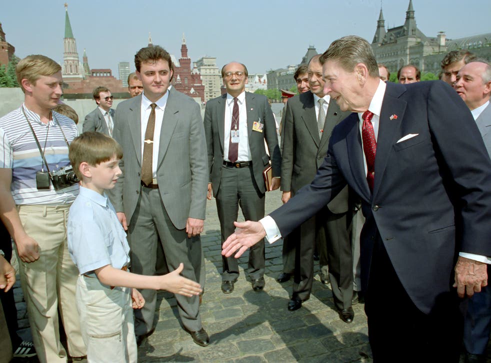 <p>Ronald Reagan le da la mano a un niño mientras Mikhail Gorbachev (der.) observa durante un recorrido por la Plaza Roja de Moscú. ¿Podría también mostrar a un joven Vladimir Putin (izq.) espiando al presidente de Estados Unidos?</p>