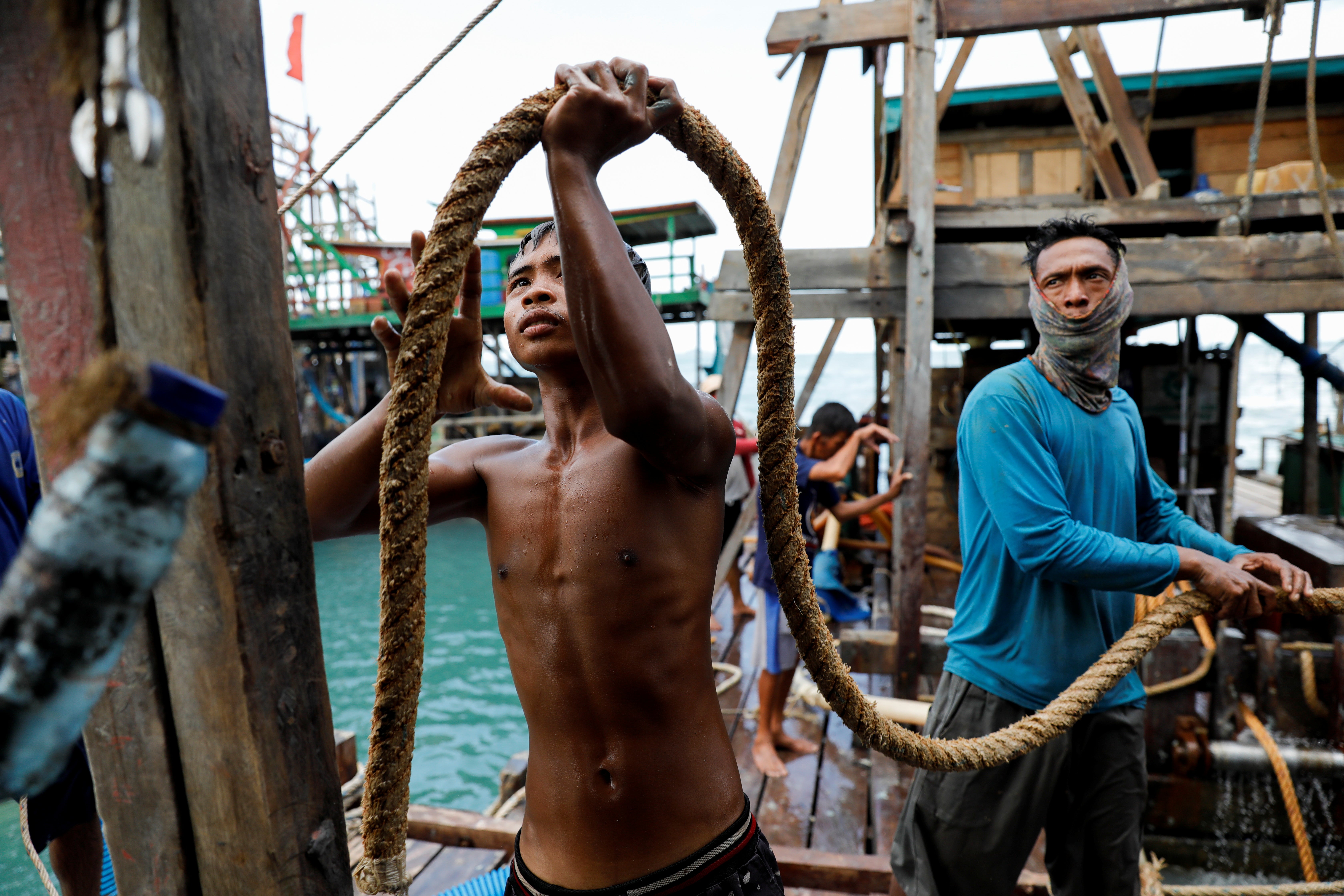 Dimas Putra Hermawan, 17, and another artisanal tin miner prepare a rope while installing a suction pipe and hose on a pontoon