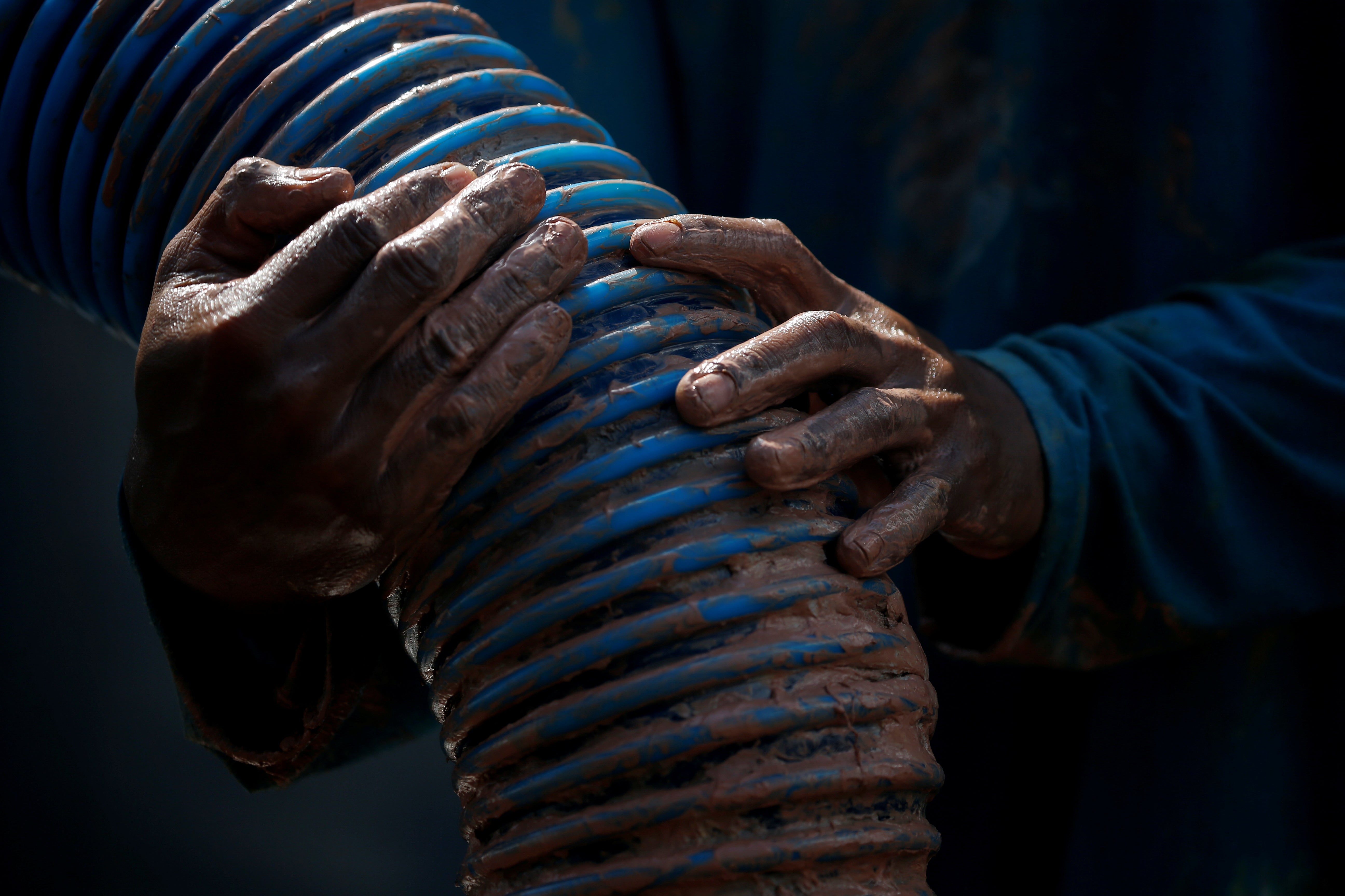 An artisanal tin miner holds a suction hose as he works on a pontoon