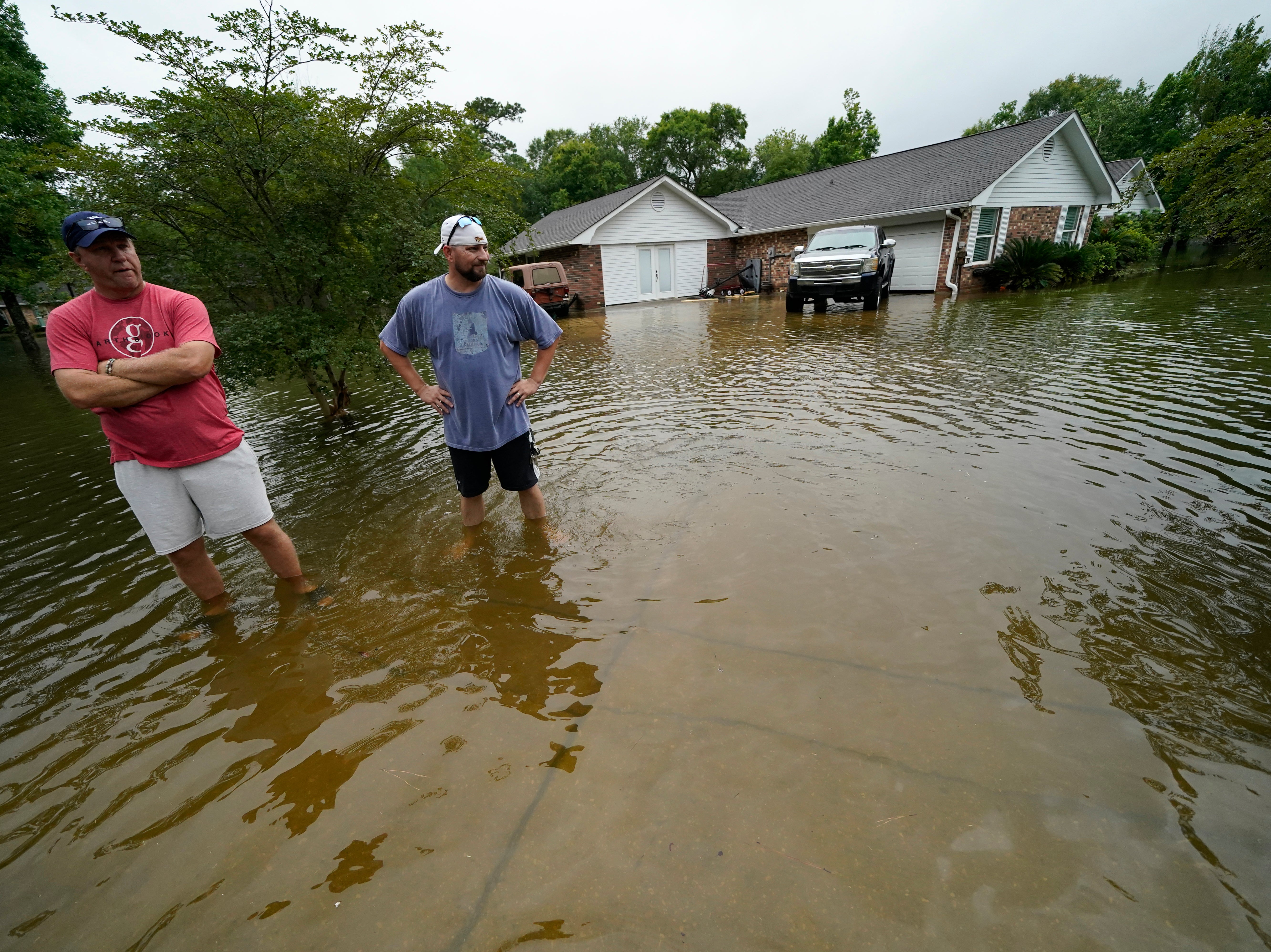 Danny Gonzales, right, stands in front of his flooded house with his neighbor Bob Neal, upset with power company trucks driving though the flooded neighborhood pushing water back into his home, after Tropical Storm Claudette passed through, in Slidell, Louisiana