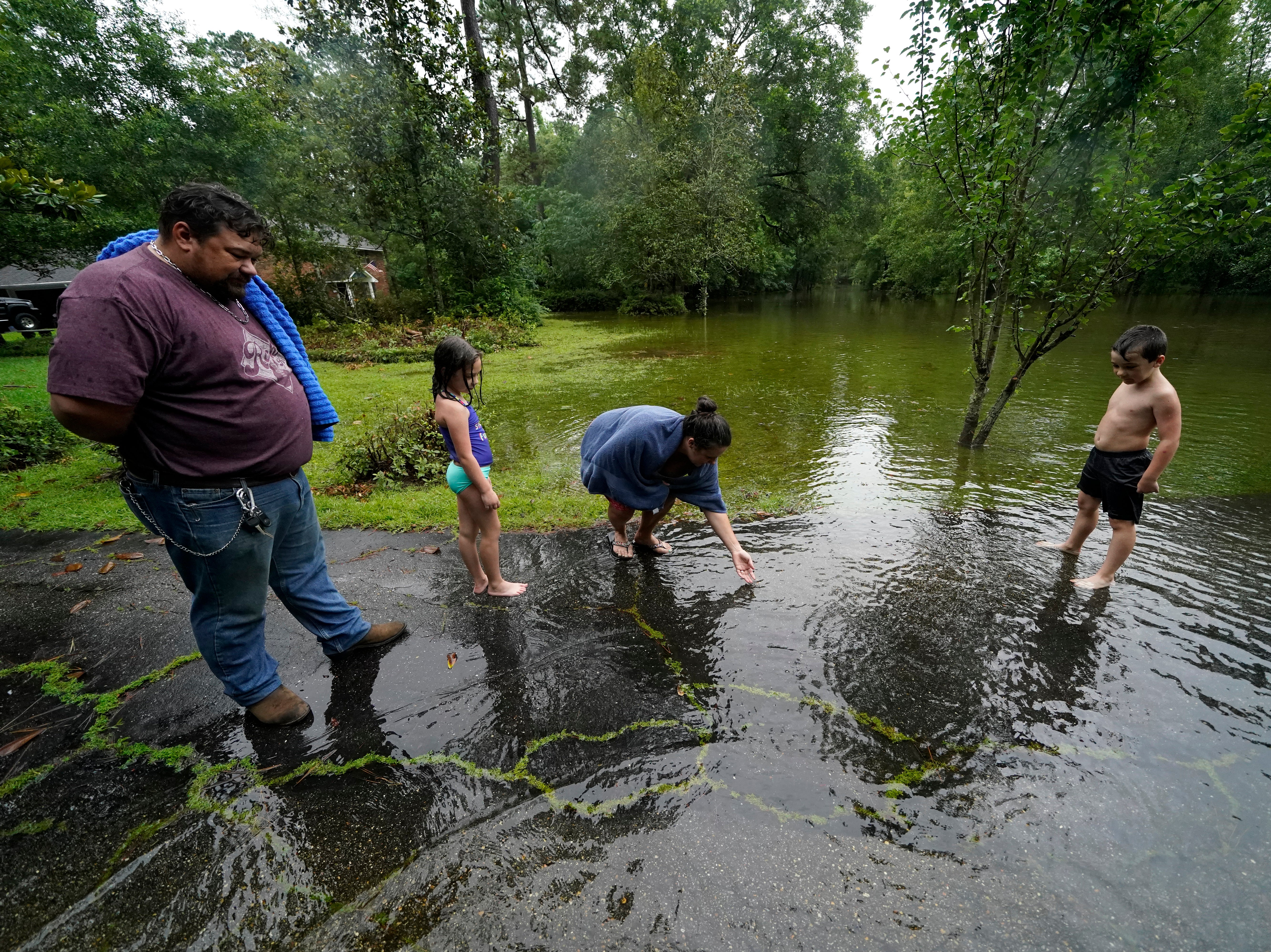 Cal Kingsmill, Jr, and his wife Jessie Kingsmill, point out crickets to their children Marina, 8, and Raylan, 8, in the receding floodwater in front of their home, after Tropical Storm Claudette passed through