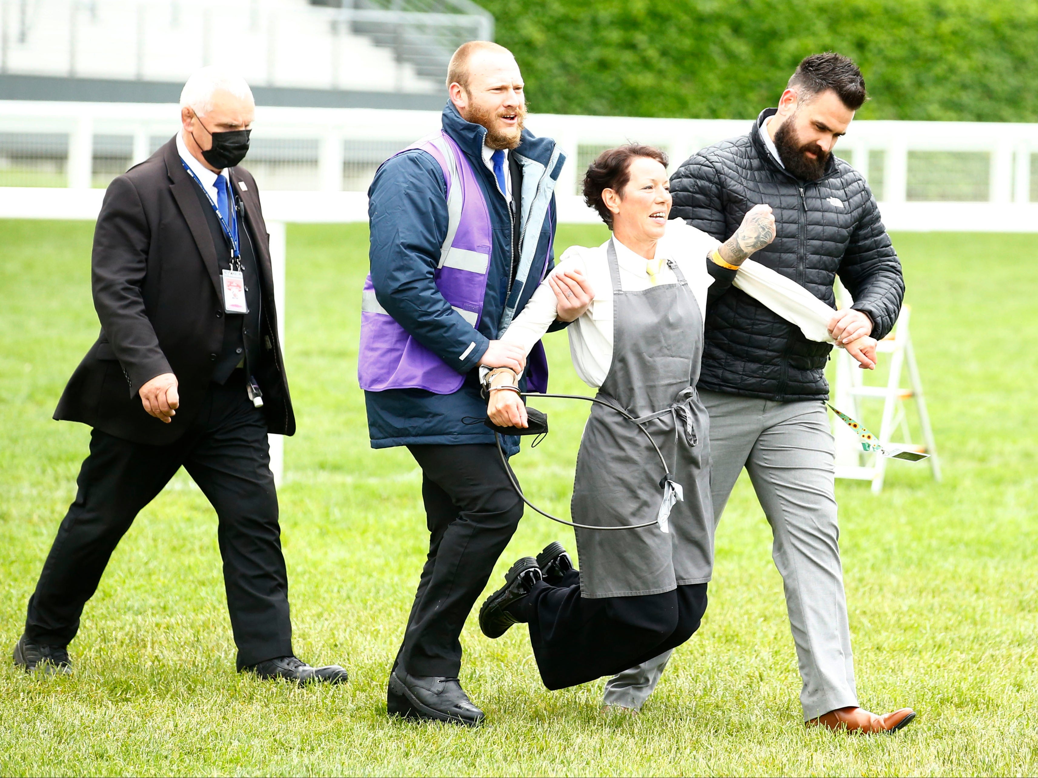 <p>An XR protestor is escorted from the racecourse during the races</p>