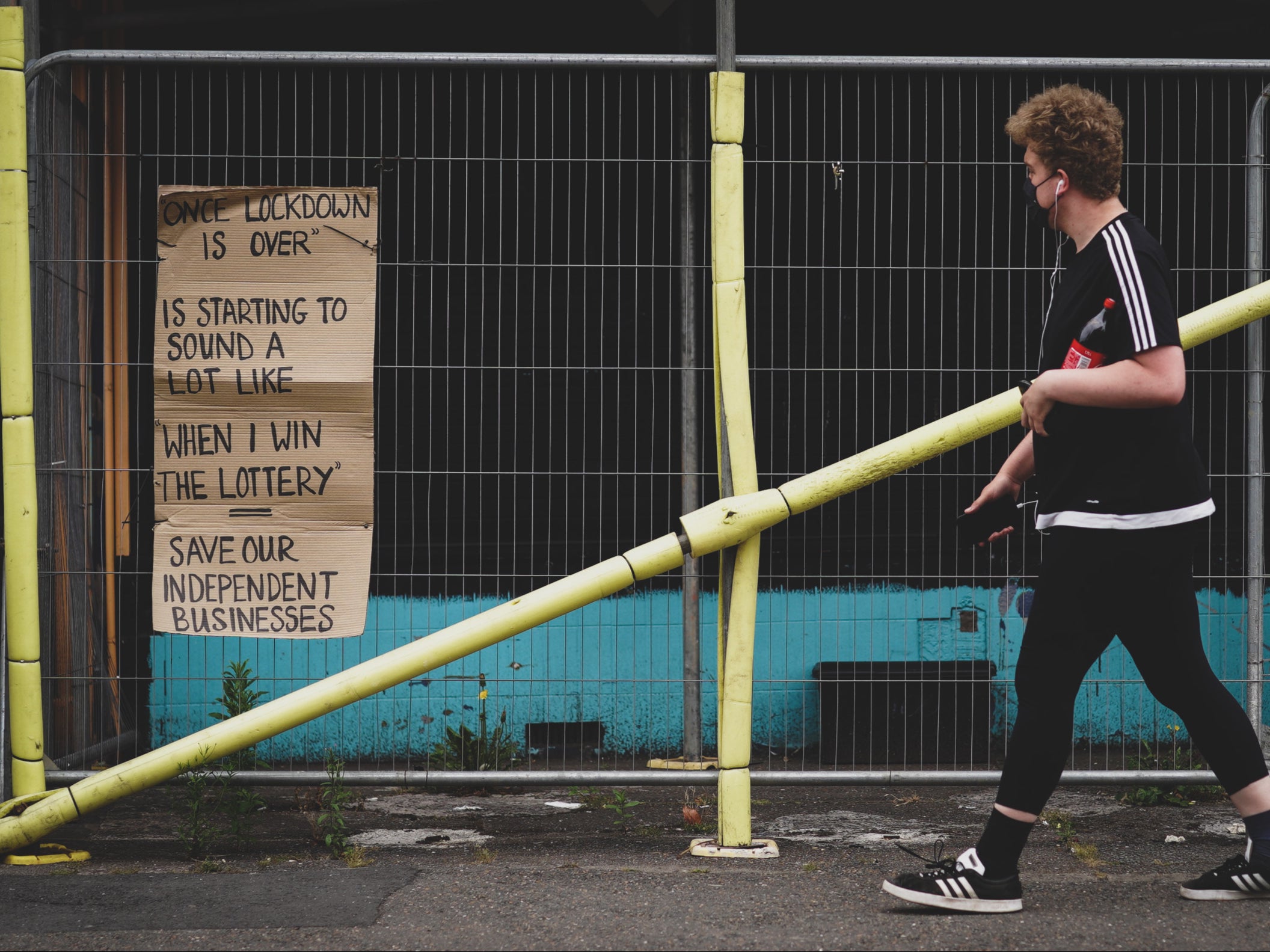 <p>A man walks past a poster referring to the end of lockdown like winning the lottery in the Totterdown area of Bristol</p>