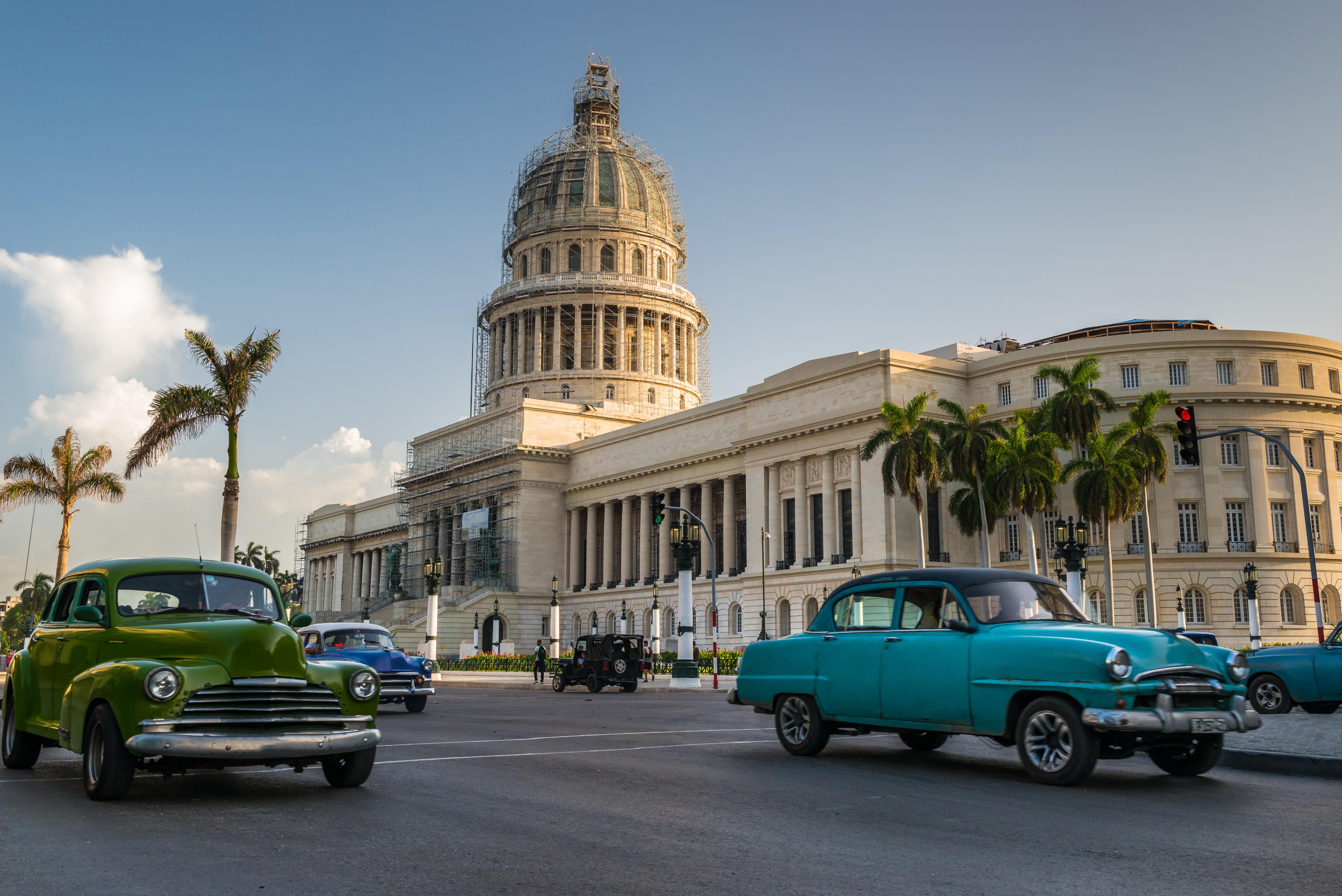 Old American cars drive past the Capitol building in Havana, Cuba
