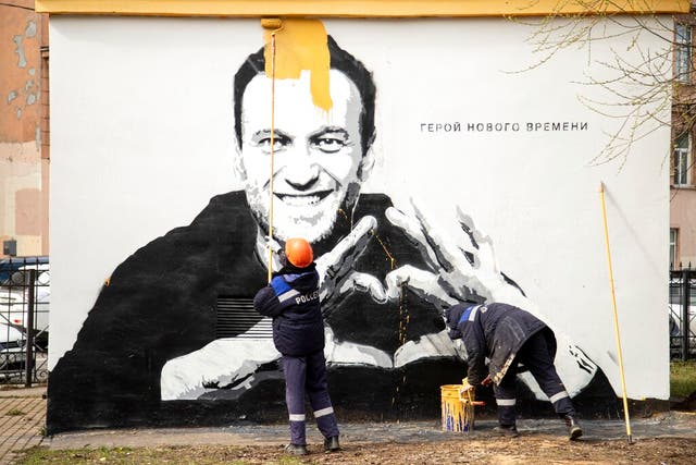 <p>Workers paint over graffiti of Alexei Navalny in St. Petersburg in April. The words on the wall reading "Hero of our time"</p>