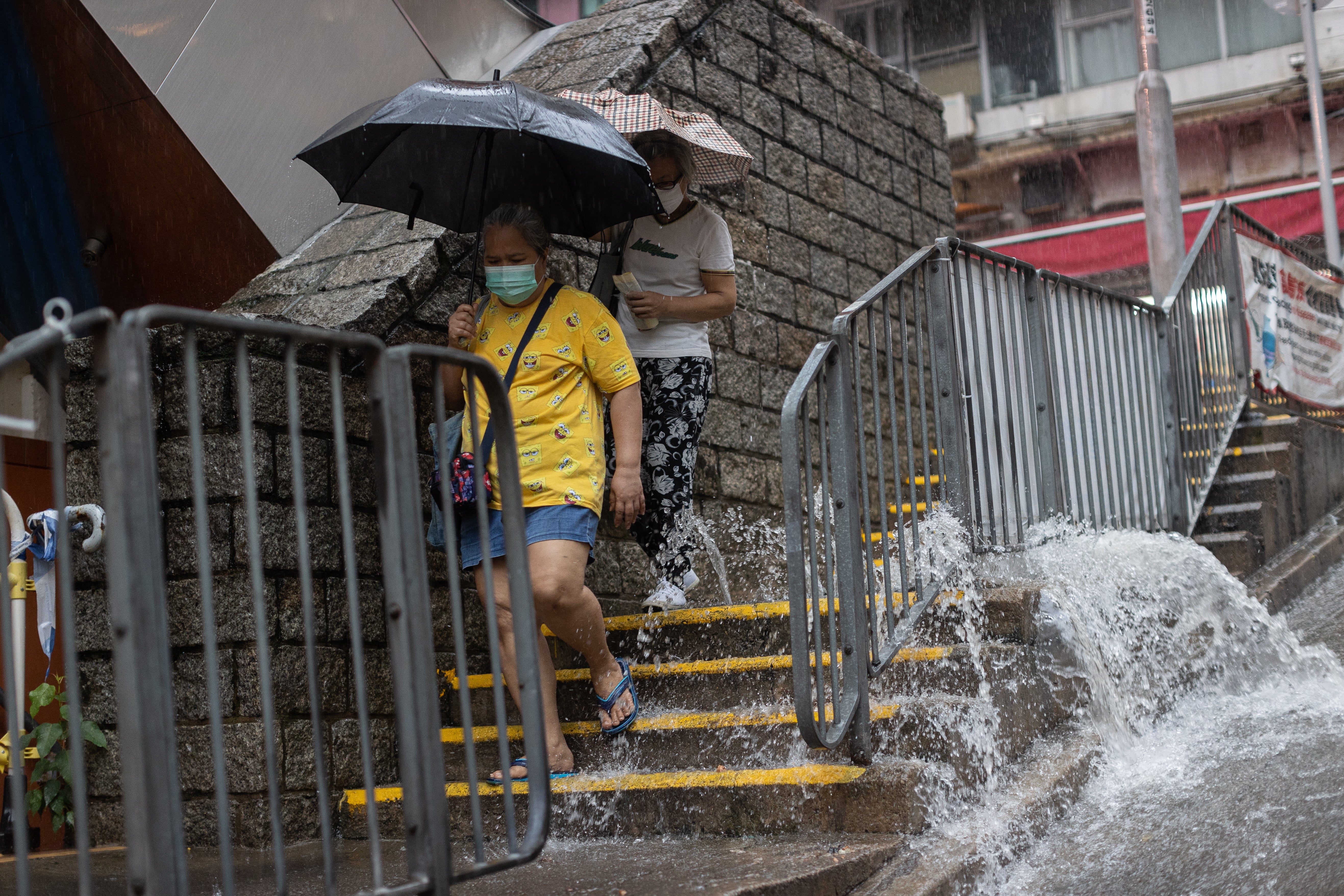 Two people walk past an overflowing manhole during a rainstorm in Hong Kong
