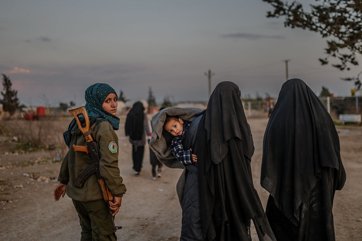 Veiled women, reportedly wives and members of Isis, walk under the supervision of a female SDF fighter at al-Hol camp