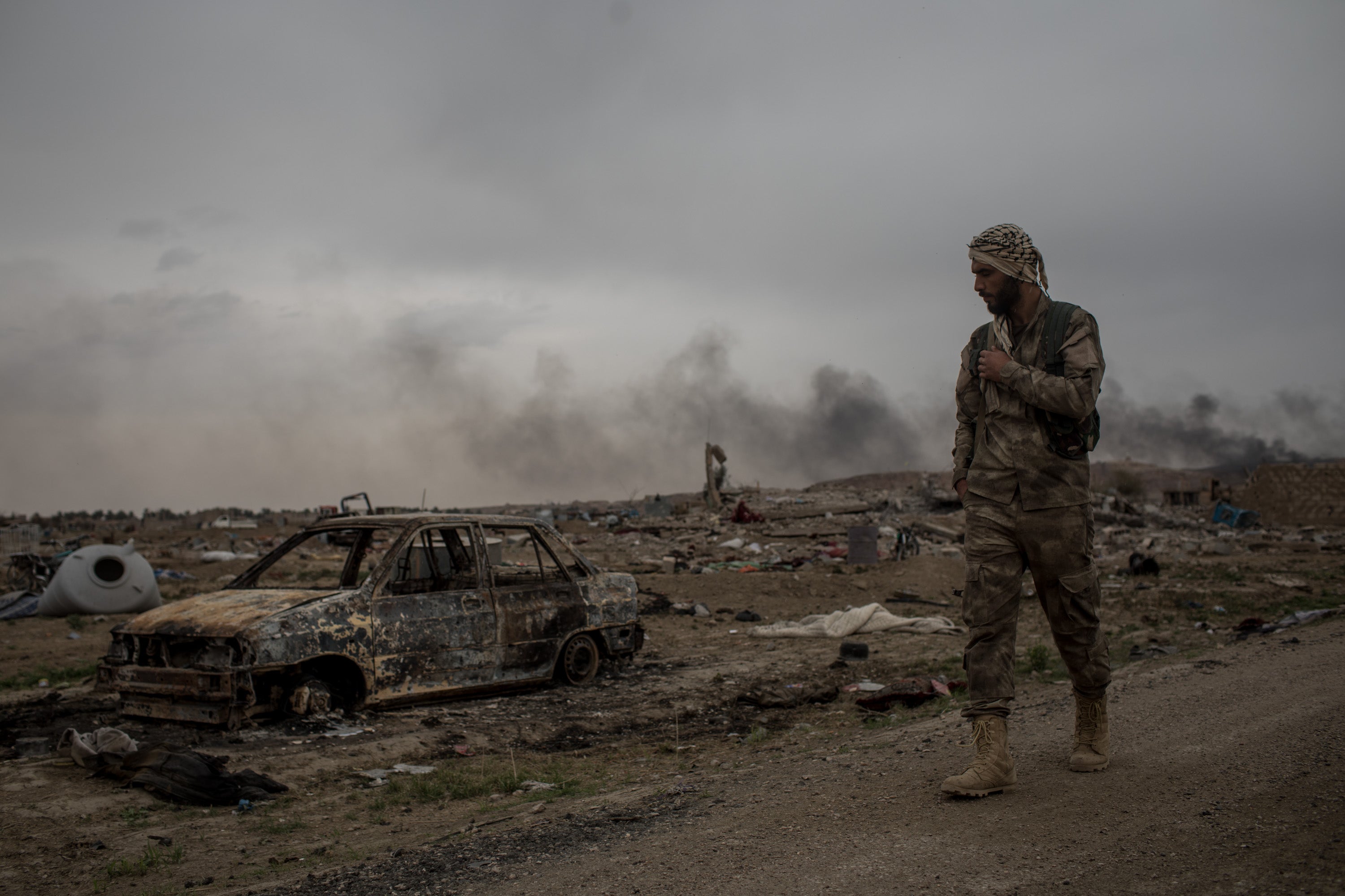 An SDF fighter walks past destroyed vehicles in the final Isis stronghold in Baghouz, after it was reclaimed in 2019