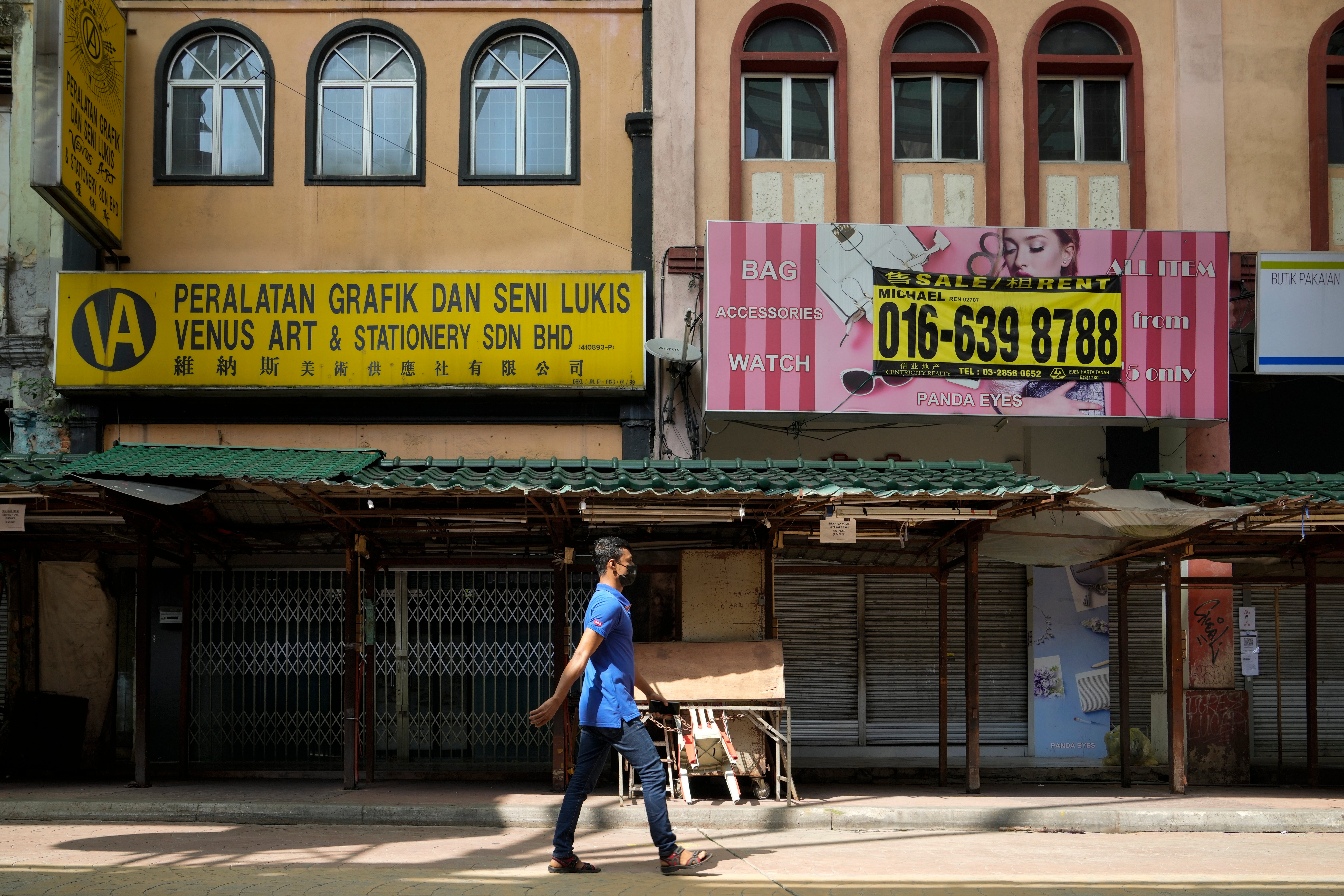 A man wearing a face mask walks by closed shops in Kuala Lumpur, Malaysia
