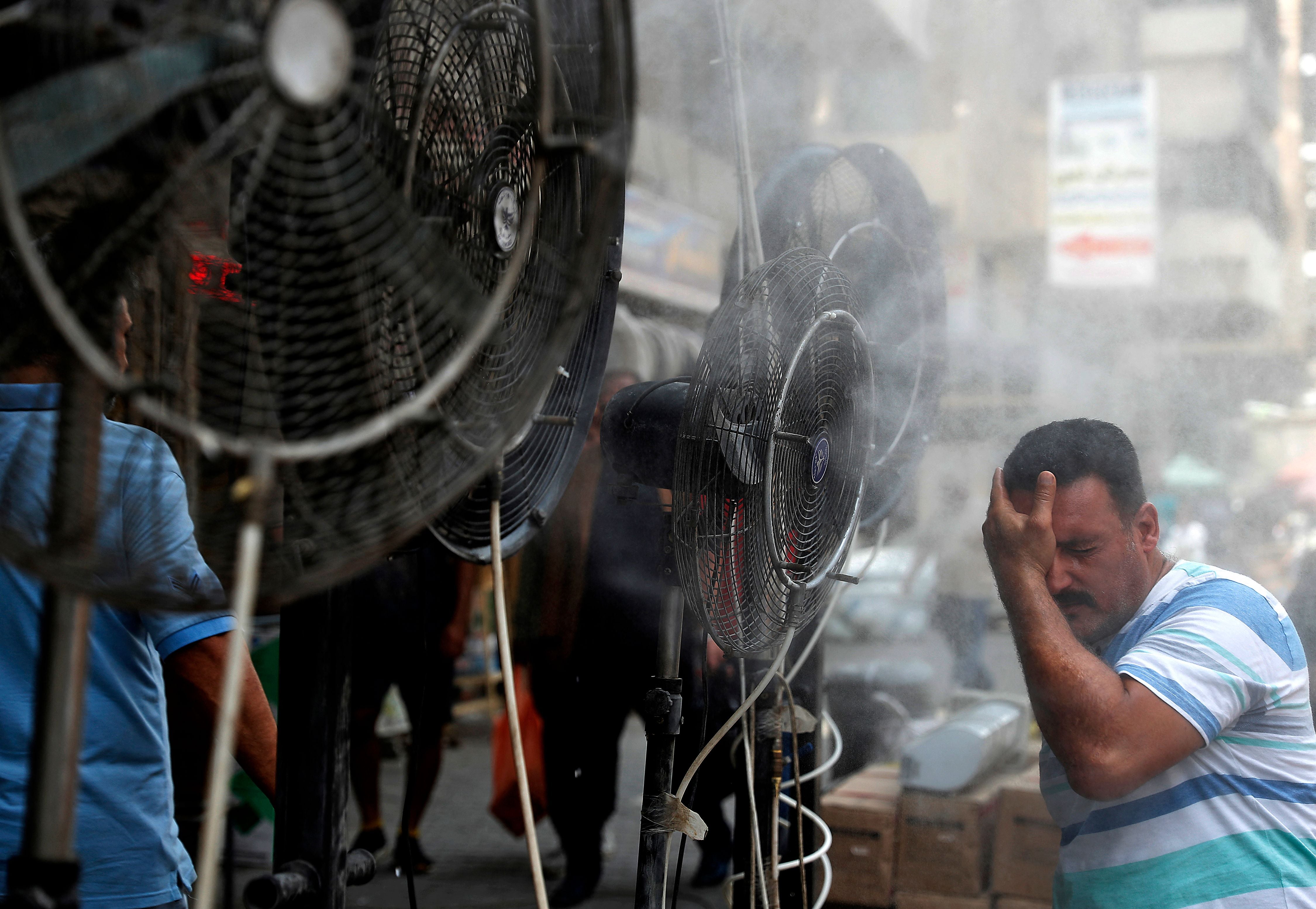 A man stands by fans spraying water vapour deployed by donors to cool down pedestrians in Iraq’s capital Baghdad