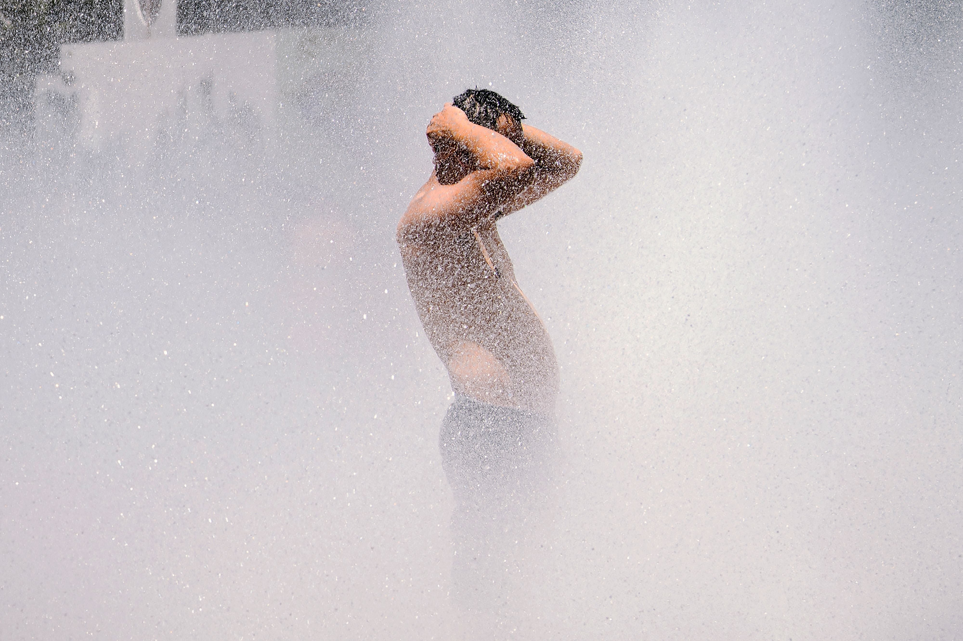 A man cools off in a street fountain in Portland, Oregon
