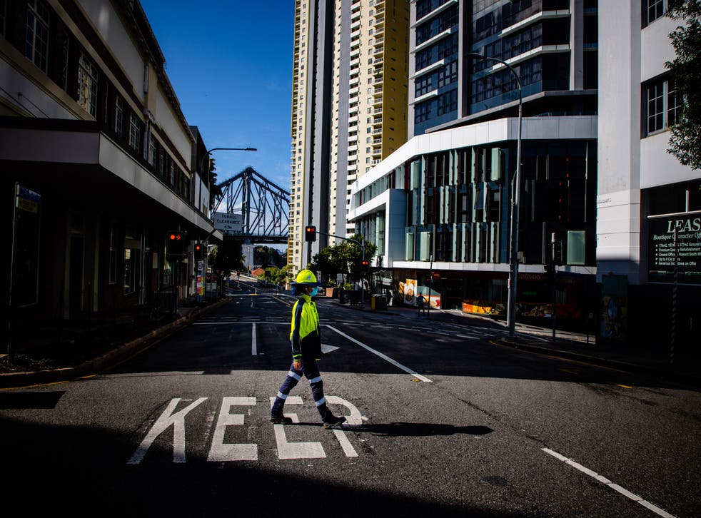 <p>A traffic control worker walks across a deserted street in Brisbane, Australia as lockdown restrictions have been extended by 72 hours for the city</p>