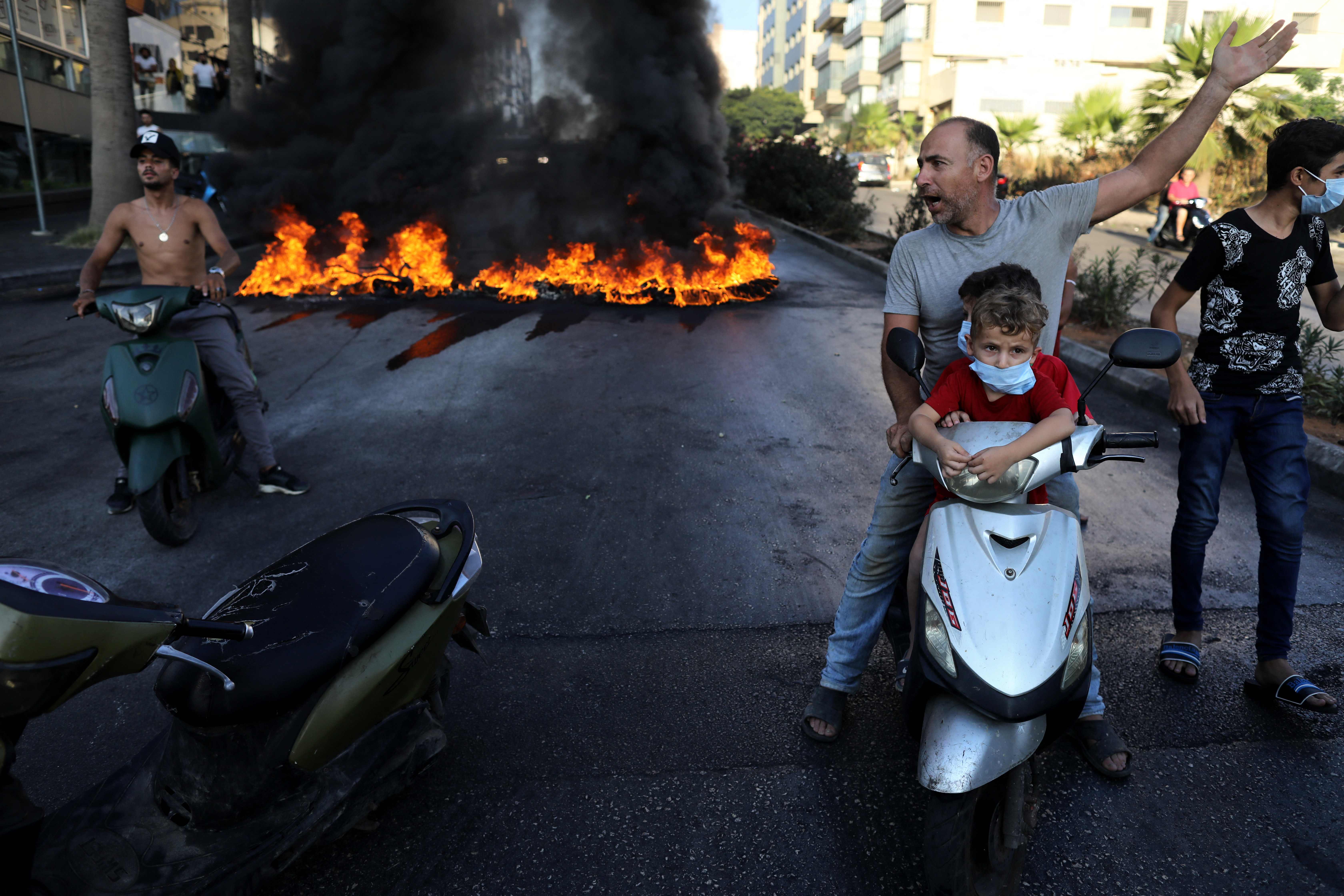 <p>A Lebanese man on a scooter with two children gestures near tires set on fire during a protest at a main road in Lebanon’s capital Beirut against dire conditions amidst the ongoing economical and political crisis</p>