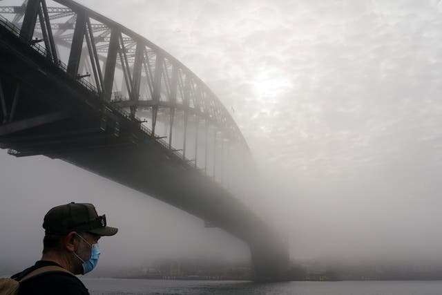 <p>Uncertain outlook. A man wearing a protective face mask next to the Sydney Harbour Bridge</p>